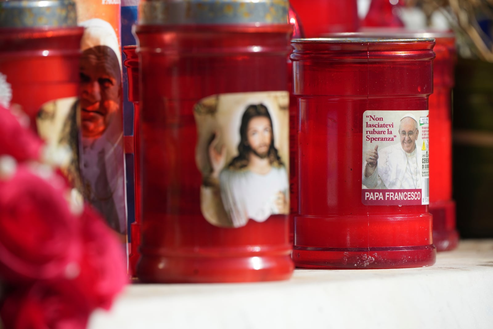 Votive candles bearing pictures of Jesus and Pope Francis with his motto in Italian: 'Don't let hope be stolen from you', are left outside the Agostino Gemelli Polyclinic in Rome, Sunday, Feb. 16, 2025, where Pope Francis was hospitalised Friday after a week-long bout of bronchitis worsened and is receiving drug therapy for a respiratory tract infection that made impossible for him to attend the traditional Sunday public blessing after the noon Angelus prayer. (AP Photo/Alessandra Tarantino)