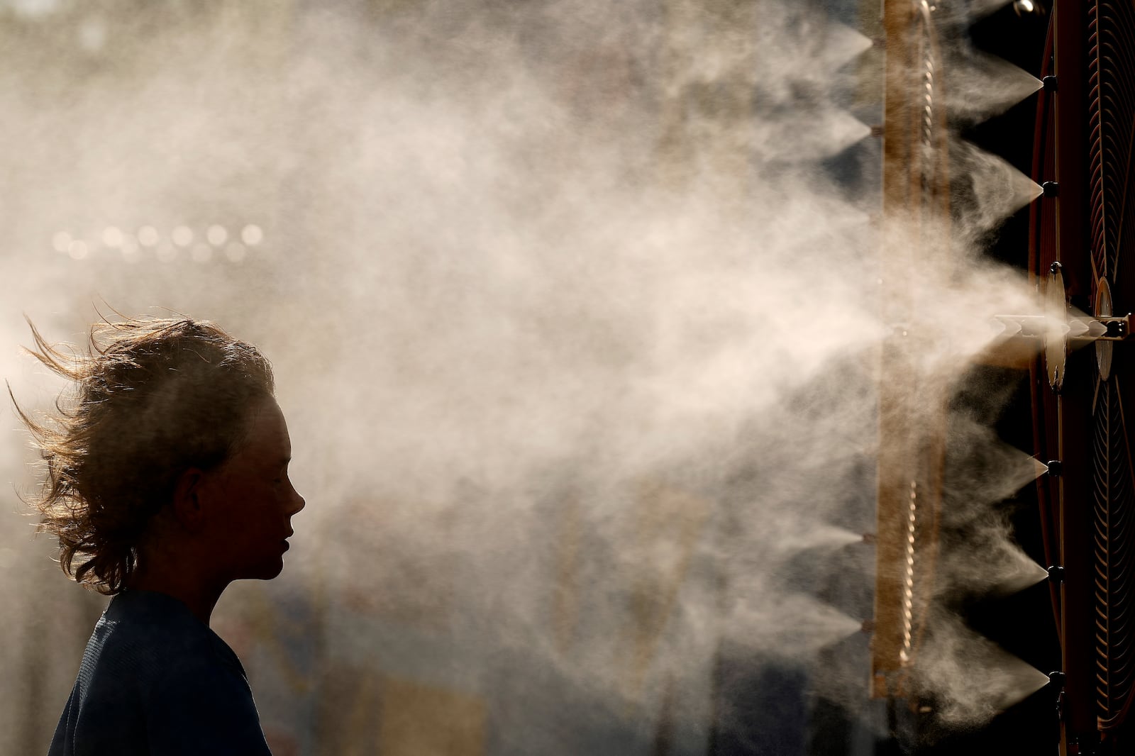 FILE - Michael Mullenax, 10, from Lee's Summit, Mo., cools off in a mister at Kauffman Stadium before a baseball game between the Kansas City Royals and the Miami Marlins, June 24, 2024, in Kansas City, Mo. (AP Photo/Charlie Riedel, File)