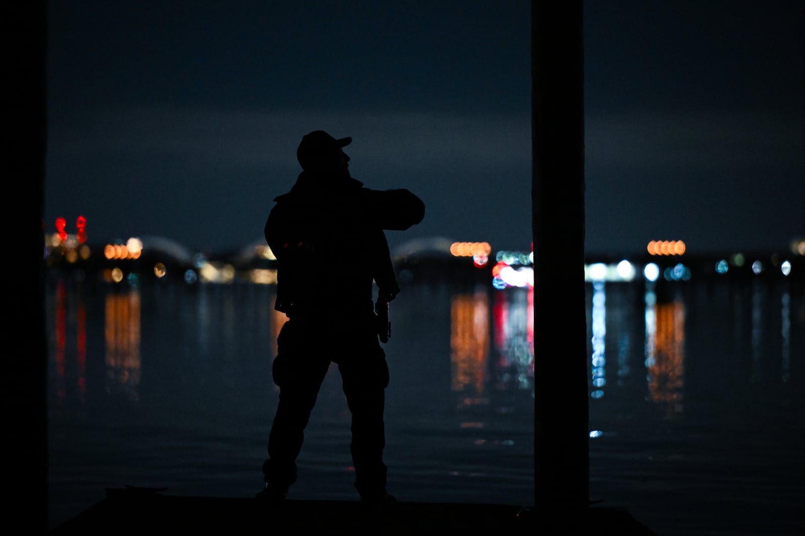 
                        An officer looks out from the end of a dock on the Potomac River during search and rescue operations after a plane crash near Ronald Reagan Washington National Airport in Arlington, Va., in the early morning hours of Thursday, Jan. 30, 2025. Many people were feared dead after a commercial jet carrying 64 people collided in midair with an Army helicopter and crashed into the Potomac River on Wednesday night. (Kenny Holston/The New York Times)
                      