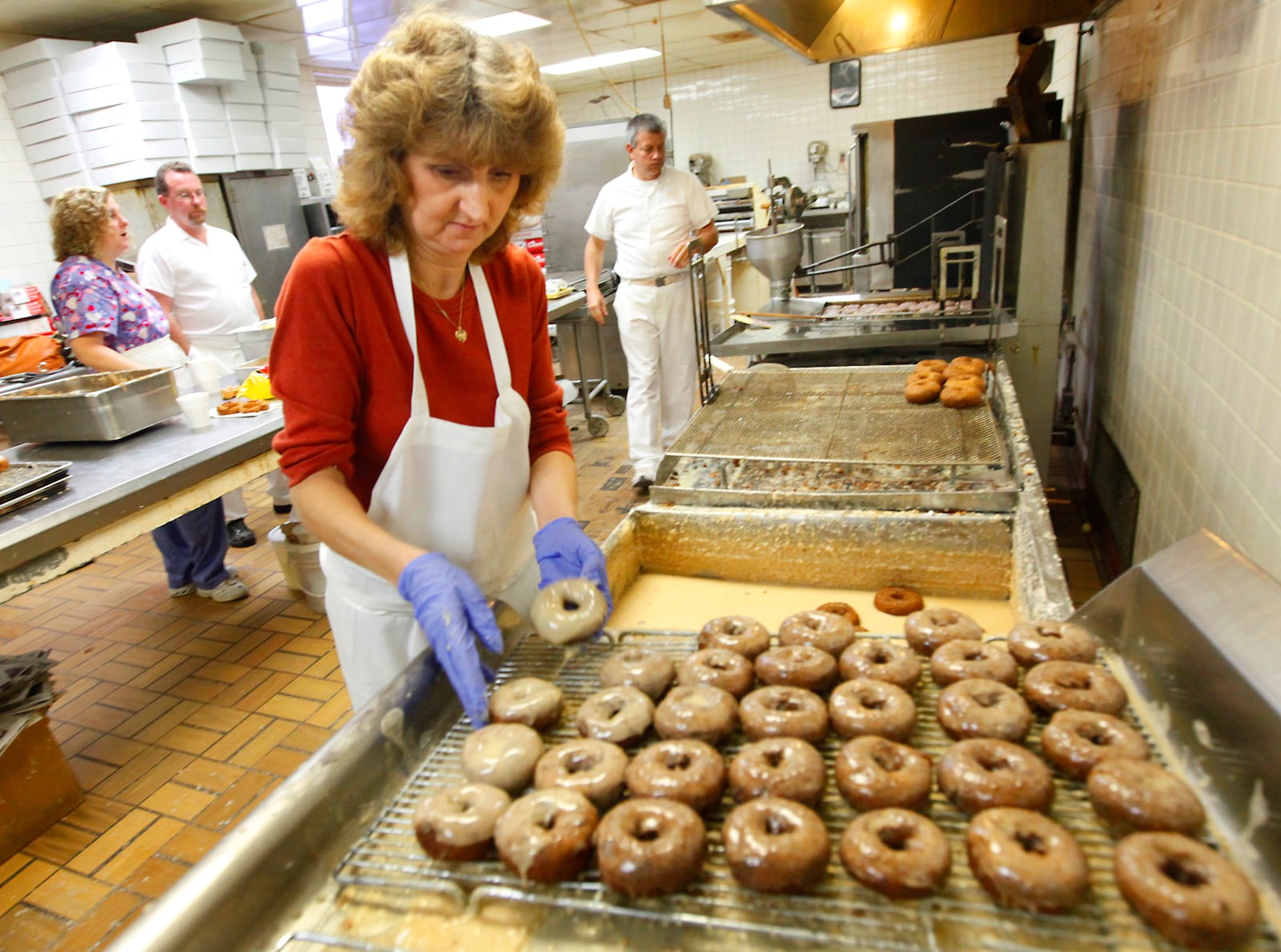 Debbie Kiser glazes blueberry donuts at Bill's Donut Shop, 268 N. Main St. Centerville. Owners Lisa Tucker and Jim Elam are in the background at left. Staff photo by Jim Witmer