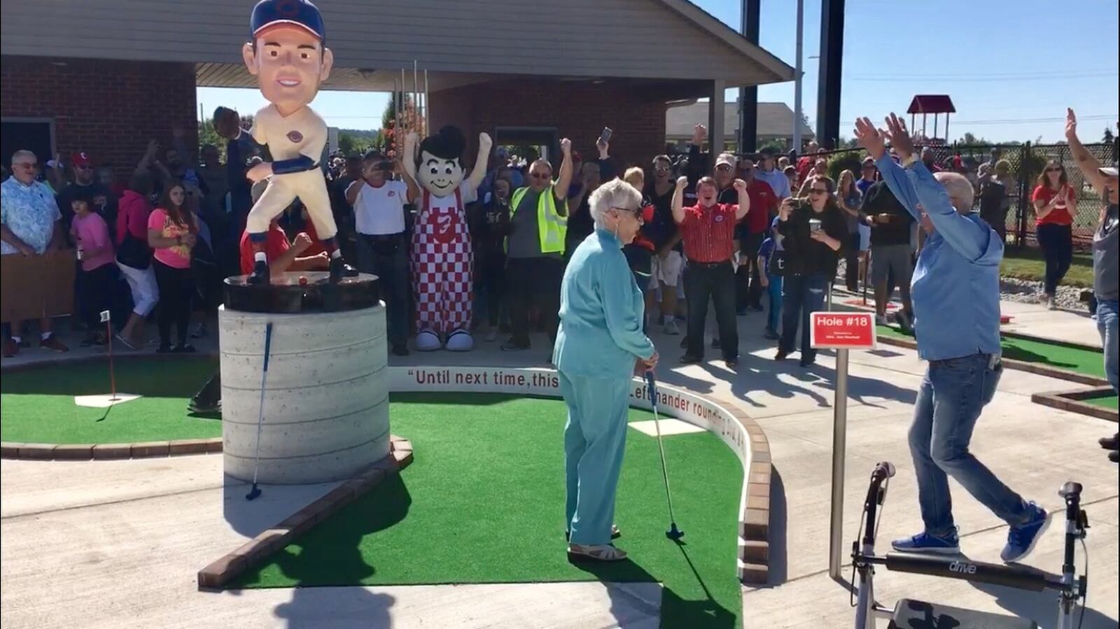 The crowd, including former Reds Hall Of Fame announcer Marty Brennaman (right), explodes as Joe Nuxhall’s widow - 91-year-old Donzetta Nuxhall - sinks the first ceremonial putt at the grand opening of the Nuxhall Miracle Fields’ mini-golf course. The Saturday opening ceremony for the special needs putt-putt course drew more than 300, including Cincinnati Reds Manager David Bell and Fairfield city officials. (Photo by Michael D. Clark/Journal-News)