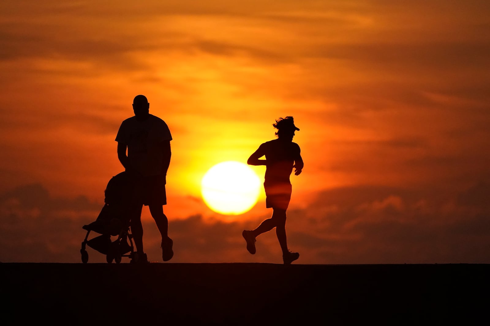 FILE - Walkers and joggers are silhouetted on a jetty as the sun rises over the Atlantic Ocean, Saturday, Sept. 19, 2020, in Bal Harbour, Fla. (AP Photo/Wilfredo Lee, File)