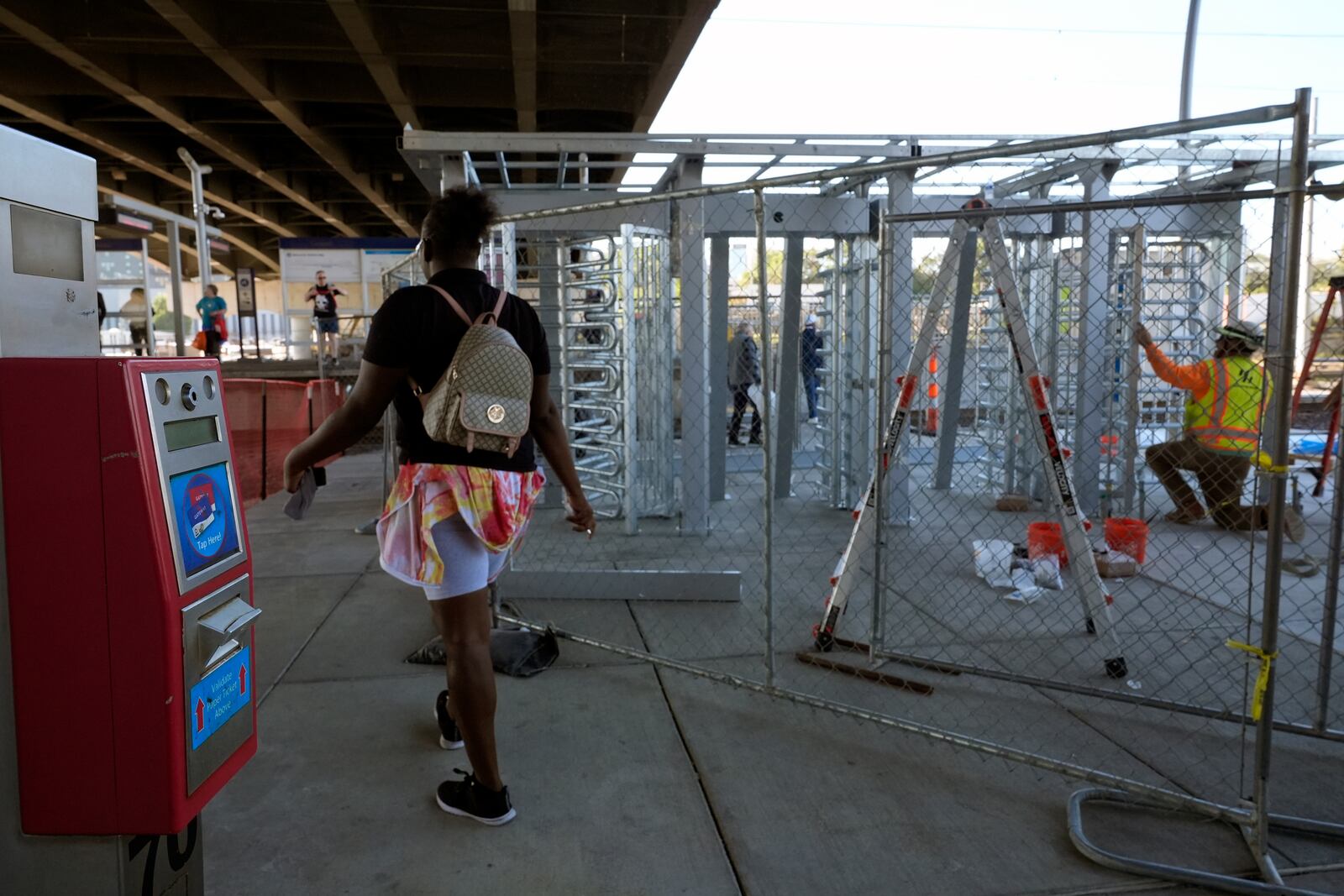 A rider passes a ticket validation scanner as workers install a metal gate that will prevent customers from entering a MetroLink platform without a valid fare card in an effort to increase security Wednesday, Oct. 9, 2024, in St. Louis. (AP Photo/Jeff Roberson)