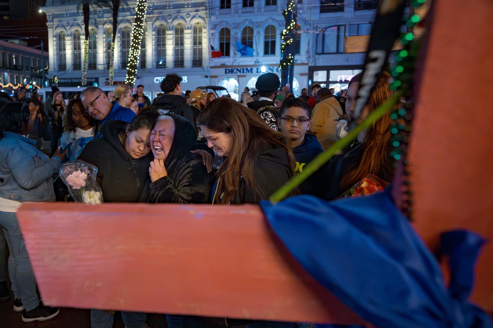 Jessica Perez, holding flowers left, hugs her mother Martha Perez who cries out by a cross memorializing her daughter, Nicole Perez, who was a victim on the New Year's Day attack, on Canal Street near the intersection of Bourbon Street in New Orleans, Saturday, Jan. 4, 2025. (AP Photo/Matthew Hinton)