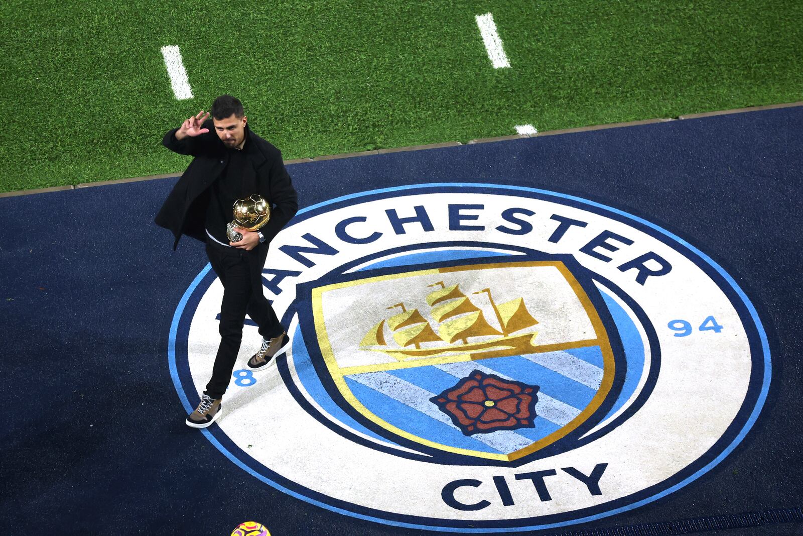 Manchester City's Rodri waves to fans with his Ballon d'Or Golden Ball trophy ahead of the British Premier League soccer match between Manchester City and Tottenham Hotspur, at the Etihad Stadium, Manchester, England, Saturday Nov. 23, 2024. (Carl Recine, Pool Photo via AP)