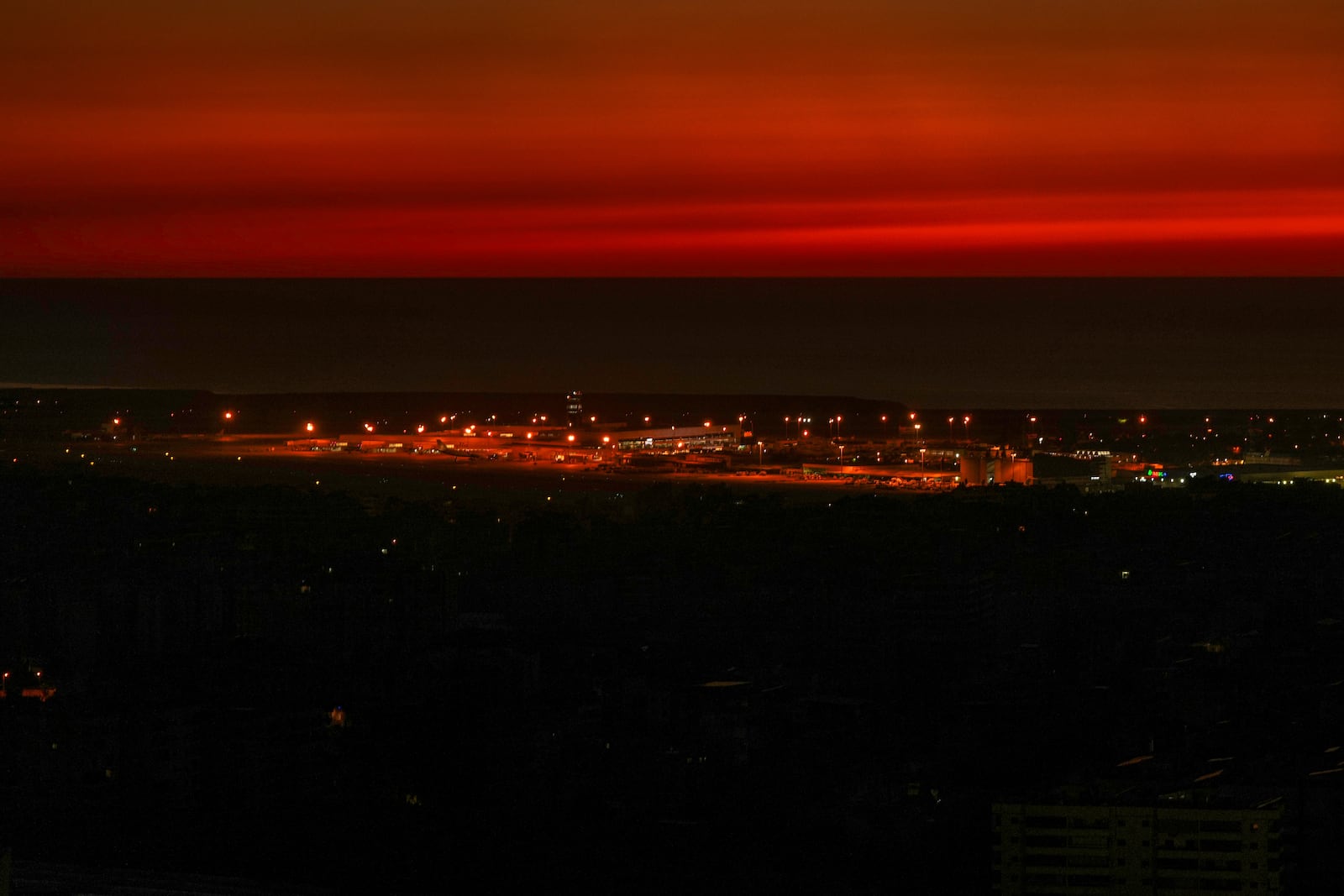 The twilight sky glows after sunset over Beirut's Rafik Hariri International Airport as Beirut's Dahiyeh suburb, foreground, remains in darkness after Israeli airstrikes, Beirut, Monday, Oct. 28, 2024. (AP Photo/Hassan Ammar)