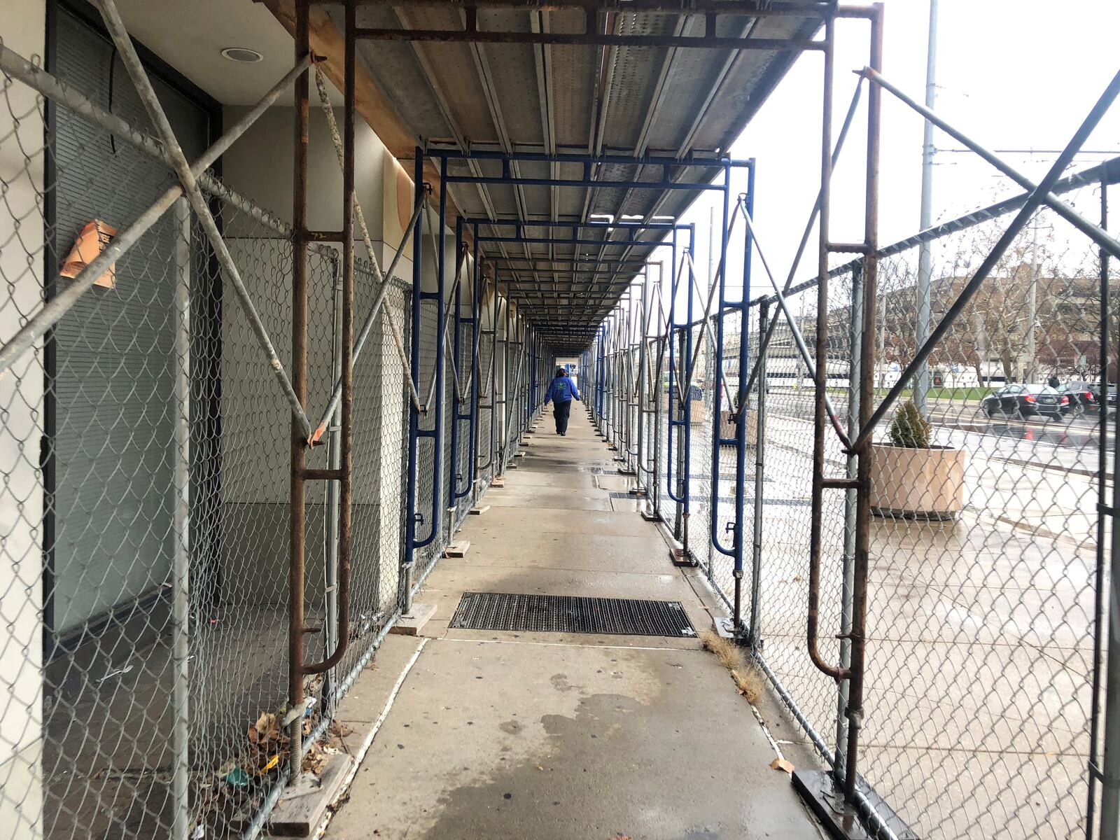 An ambassador with the Downtown Dayton Partnership walks through the covered pedestrian walkway along the Centre City building that uses scaffolding to protect people from falling materials. The building, at South Main and East Fourth streets, is in severe disrepair. CORNELIUS FROLIK / STAFF