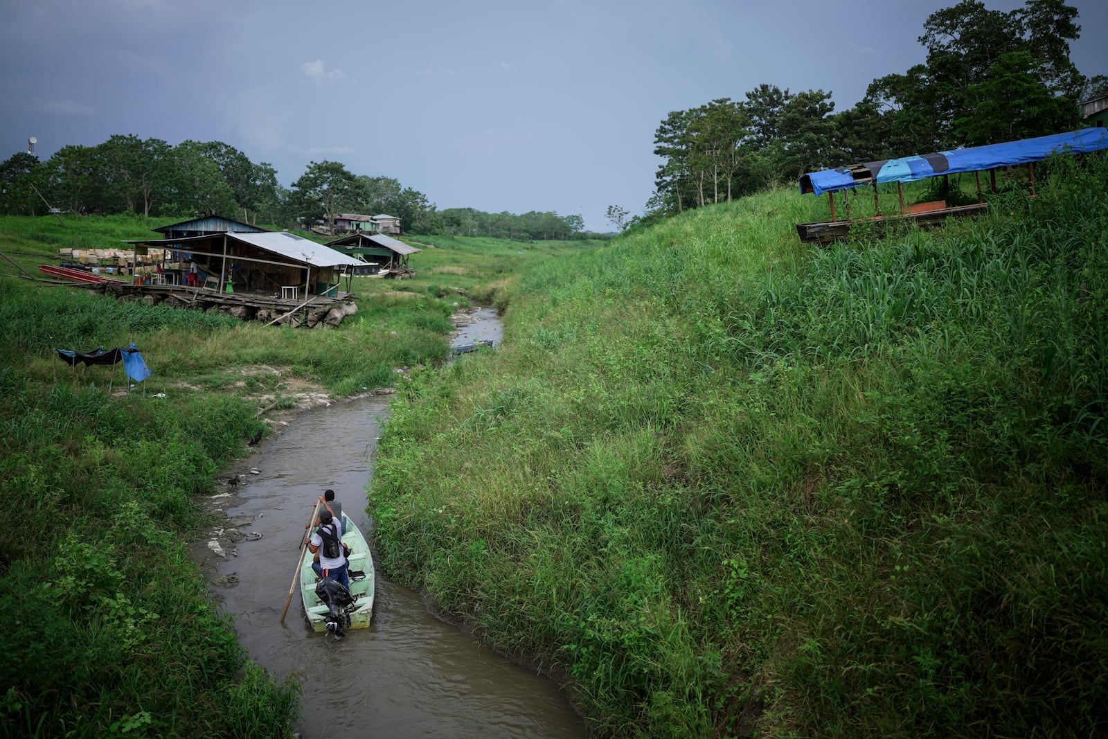 People maneuver by boat through the low level of a tributary that connects with the Amazon River, in Isla de la Fantasia, on the outskirts of Leticia, Colombia, Sunday, Oct. 20, 2024. (AP Photo/Ivan Valencia)