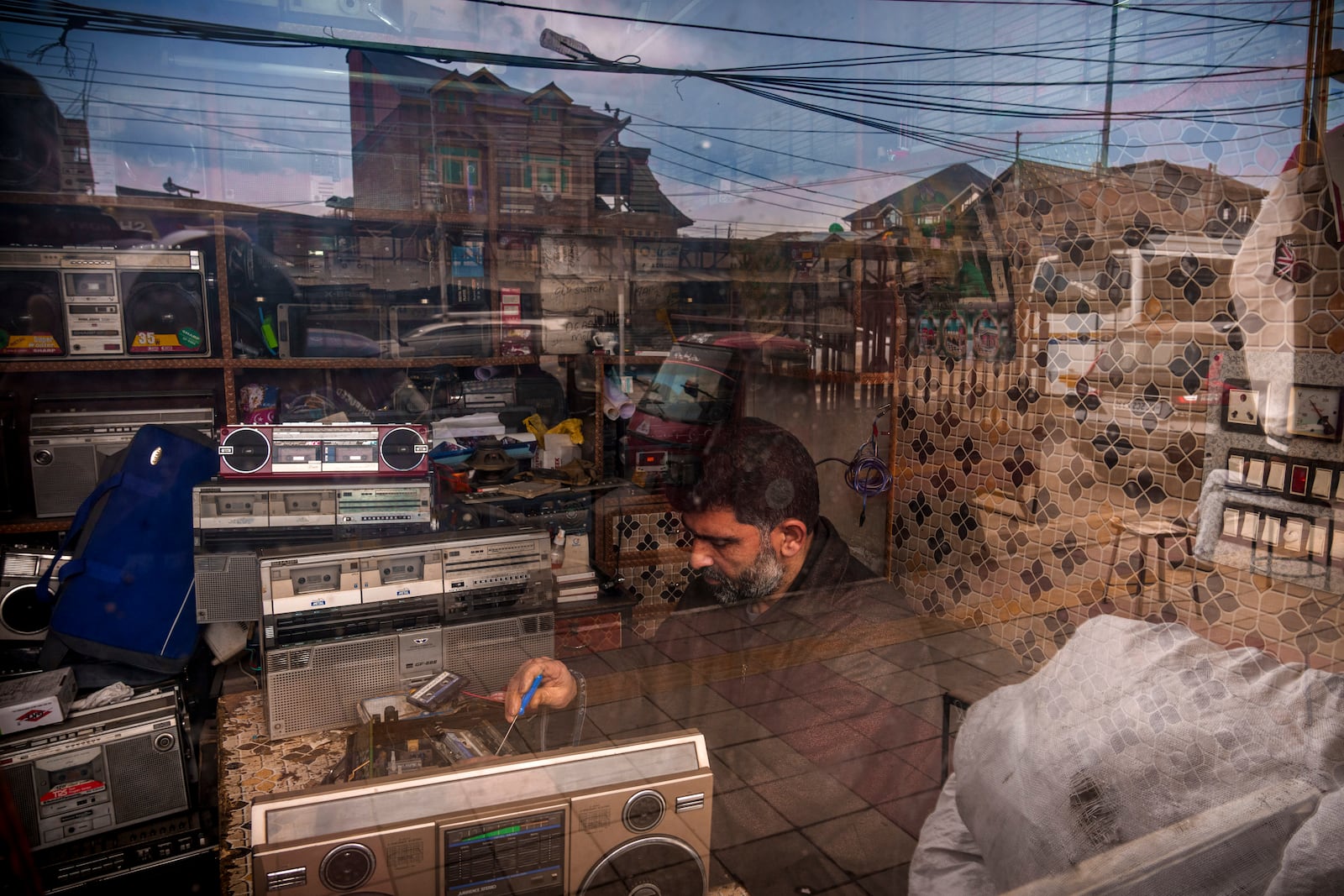 Self-taught tape recorder mechanic Mohammad Ashraf Matoo is seen through a glass window as he repairs a tape recorder at his shop in Srinagar, Indian controlled Kashmir, Tuesday, Feb. 11, 2025. (AP Photo/Dar Yasin)