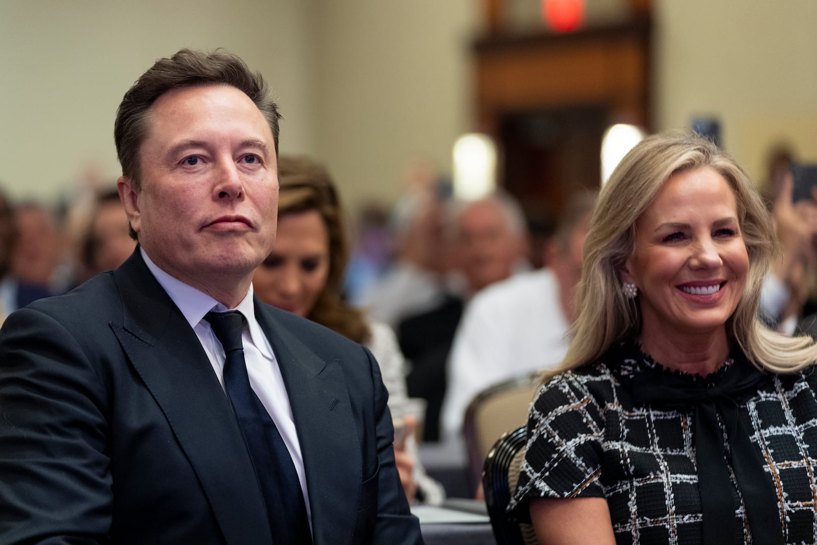 Elon Musk, left, sits with Kelly Johnson, wife of House Speaker Mike Johnson of La., as President-elect Donald Trump speaks at a meeting of the House GOP conference, Wednesday, Nov. 13, 2024, in Washington. (AP Photo/Alex Brandon)