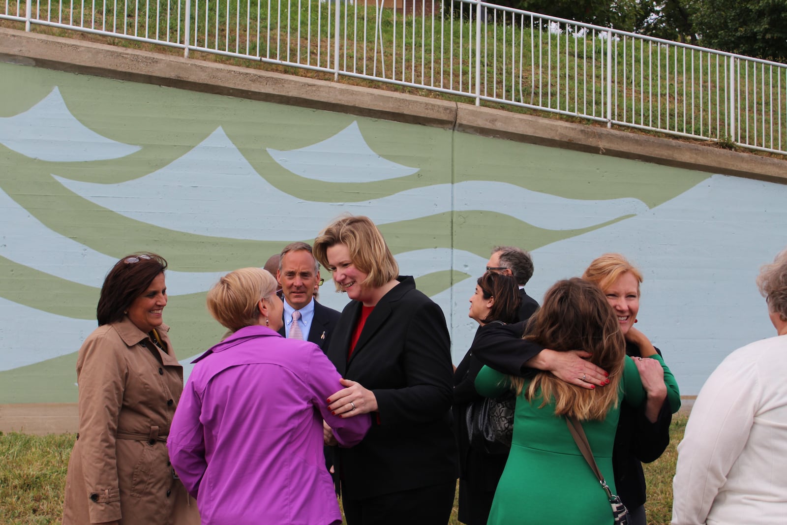 Dozens gathered on the north side of the Great Miami River for the Oct. 1, 2015, ribbon-cutting for the newly painted River Run Floodwall, including local elected officials like Dayton Mayor Nan Whaley and Downtown Dayton Partnership President Sandy Gudorf and art professionals from around the region and downtown Dayton supporters. Designed by local artist and graphic designer Amy Deal, the nearly 1,000-foot floodwall is part of the signature project, RiverScape River Run, of  the Greater Downtown Dayton Plan. VIVIENNE MACHI / STAFF