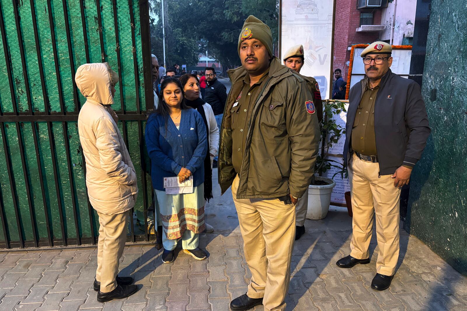 People stand in a queue to cast their votes for the capital’s state legislature election as policemen stand guard at a polling booth in New Delhi, India, Wednesday, Feb. 5, 2025. (AP Photo/Shonal Ganguly)