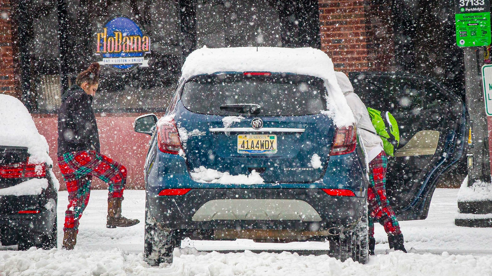 A woman kicks her tires to clear snow after parking along North Court Street as snow falls, Friday, Jan. 10, 2025, in Florence, Ala. (Dan Busey/The TimesDaily via AP)