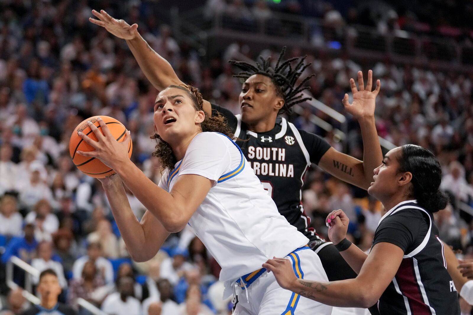 Left to right, UCLA center Lauren Betts, left, drives to the basket against South Carolina forward Ashlyn Watkins, center, and guard Te-Hina Paopao, right, during the second half of an NCAA college basketball game, Sunday, Nov. 24, 2024, in Los Angeles. (AP Photo/Eric Thayer)