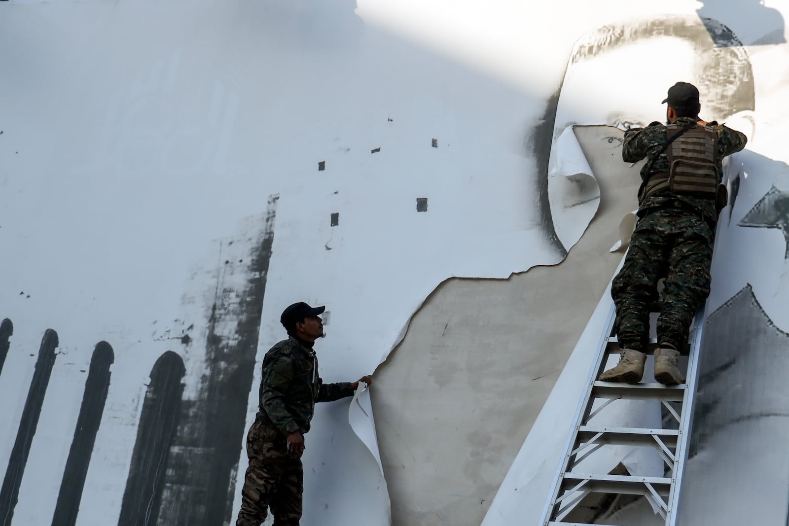 Syrian opposition fighters remove a sign with a picture of Syrian President Bashar Assad at the Aleppo international airpot in Aleppo, Syria, Monday, Dec. 2, 2024. .(AP Photo/Omar Albam)