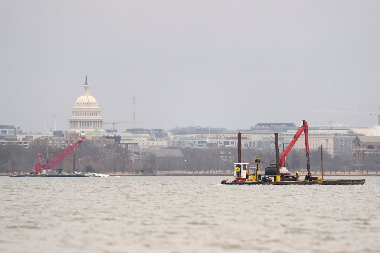 With the U.S. Capitol in the background, cranes are pictured in the Potomac river Sunday, Feb. 2, 2025, near the wreckage of an American Airlines jet, at left, that collided mid-air with an Army Black Hawk helicopter in Arlington, Va., as seen from Alexandria, Va. (AP Photo/Carolyn Kaster)