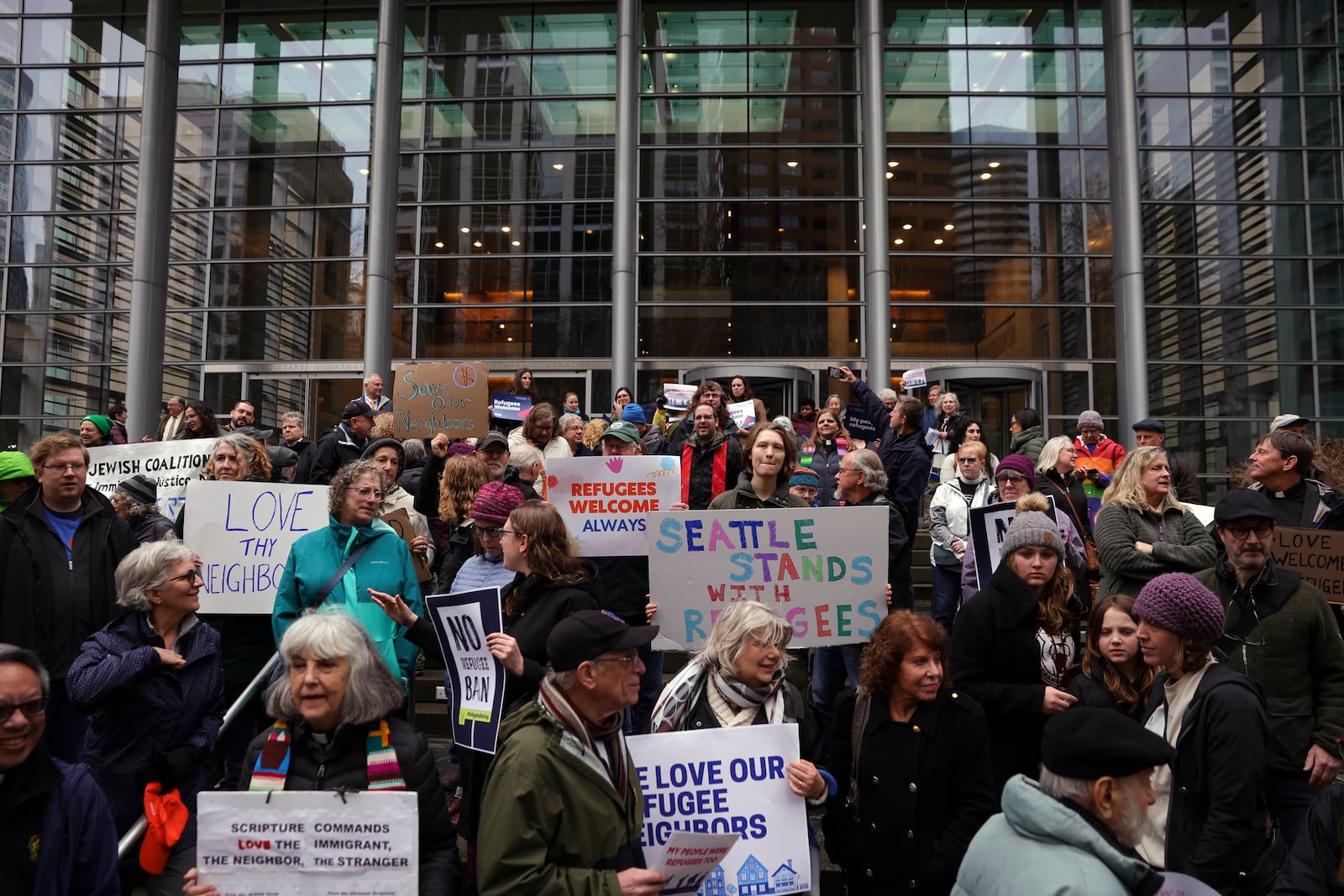 People hold signs as they gather outside the U.S. District Court after a federal judge blocked President Donald Trump's effort to halt the nation's refugee admissions system Tuesday, Feb. 25, 2025, in Seattle. (AP Photo/Ryan Sun)