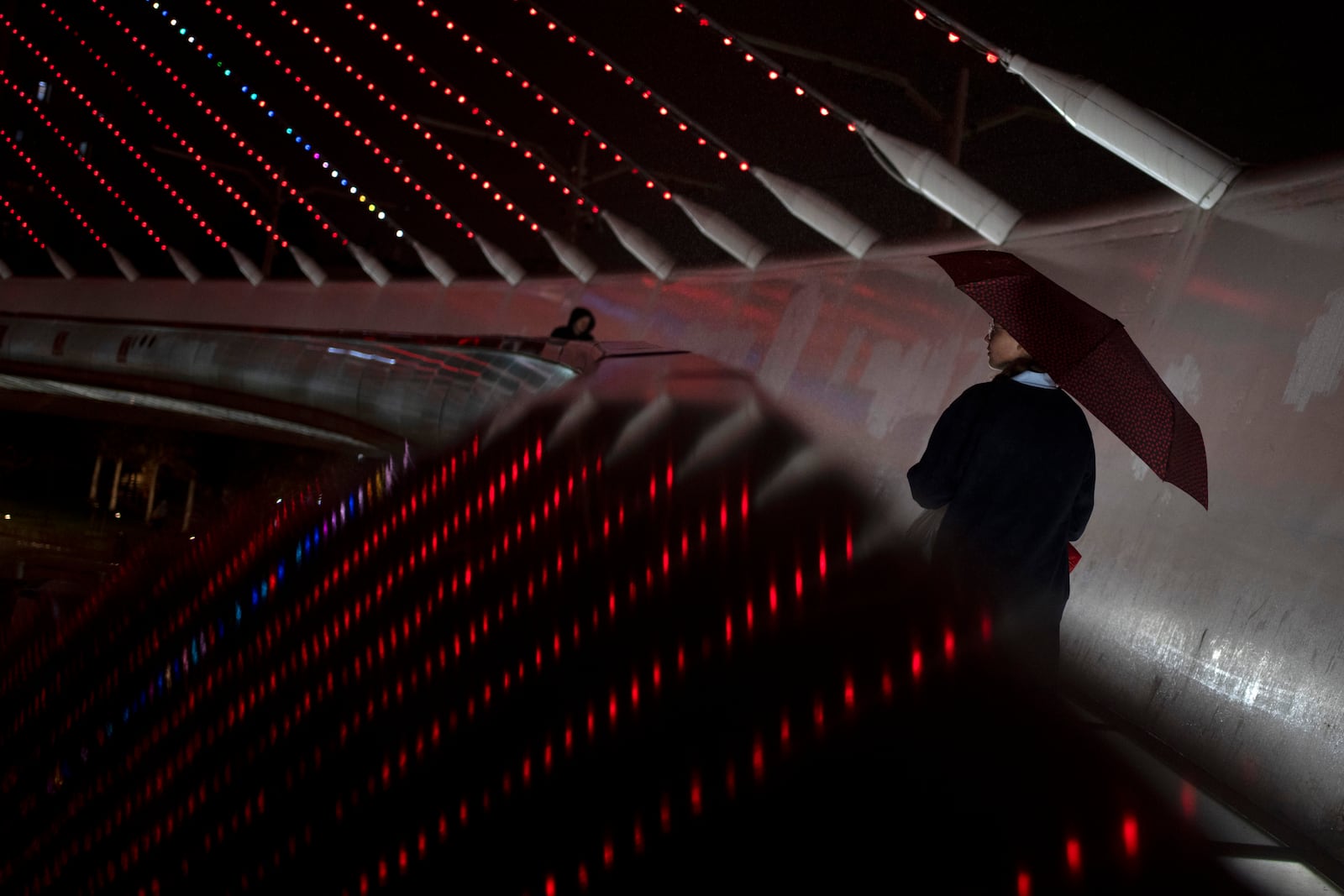 A young woman walks on the Chords Bridge at the entrance to Jerusalem, illuminated in red to mark the International Day for the Elimination of Violence Against Women, Monday, Nov. 25, 2024. (AP Photo/Maya Alleruzzo)