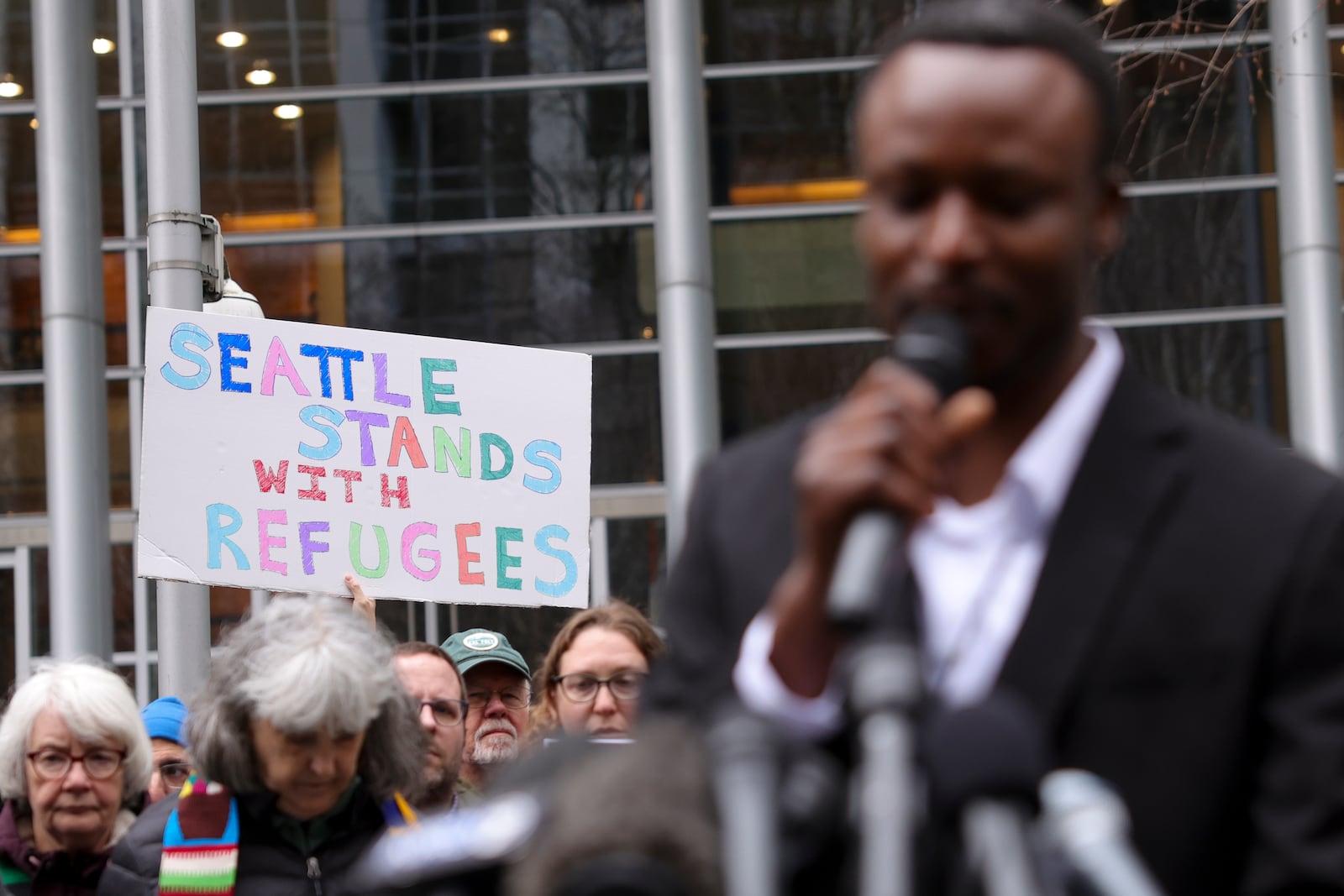 Signs are seen as Tshishiku Henry, a former refugee and Washington State Delegate for the Refugee Congress, speaks during a rally outside the U.S District Court after a federal judge blocked President Donald Trump's effort to halt the nation's refugee admissions system, Tuesday, Feb. 25, 2025 in Seattle. (AP Photo/Ryan Sun)