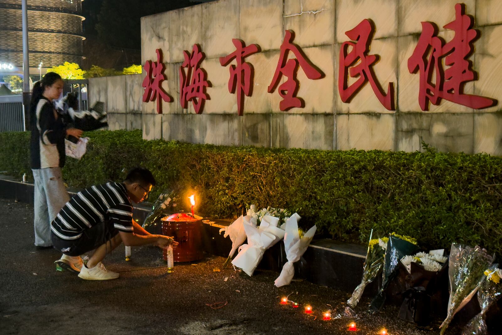 A man lights a candle near flowers placed outside the Zhuhai People's Fitness Plaza, where a man deliberately rammed his car into people exercising at the sports center, killing some and injuring others in Zhuhai in southern China's Guangdong province on Tuesday, Nov. 12, 2024. (AP Photo/Ng Han Guan, File)