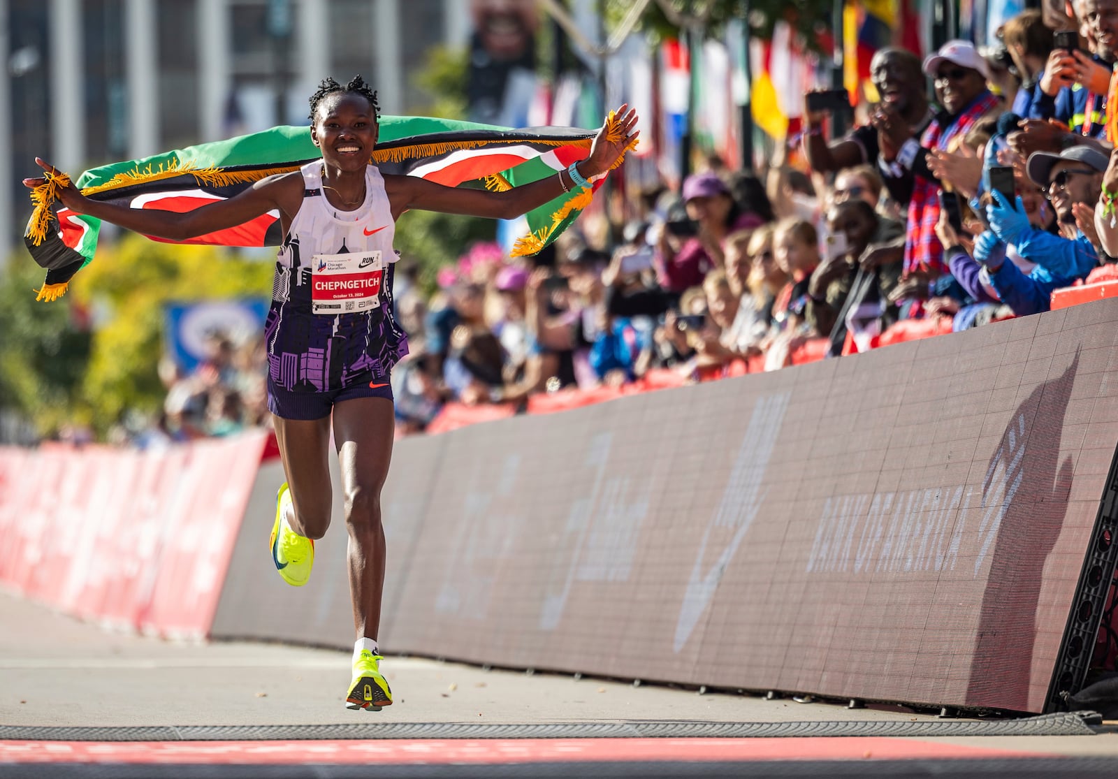 Ruth Chepngetich, from Kenya, runs with the Kenyan flag after crossing the finish line of the Chicago Marathon to win the women's professional division and break the women's marathon world record in Grant Park, Sunday, Oct. 13, 2024. (Tess Crowley/Chicago Tribune via AP)