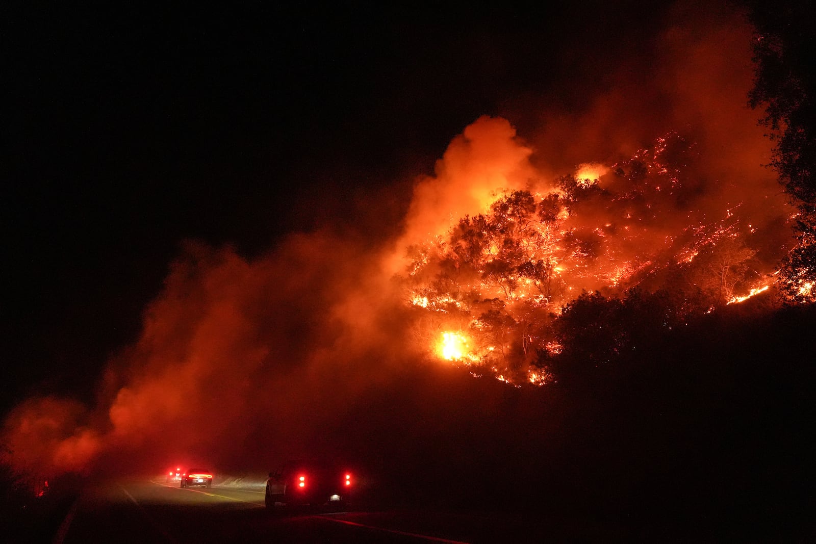 Vehicles pass through smoke from the Lilac Fire in Bonsall, Calif., Tuesday, Jan. 21, 2025. (AP Photo/Jae C. Hong)