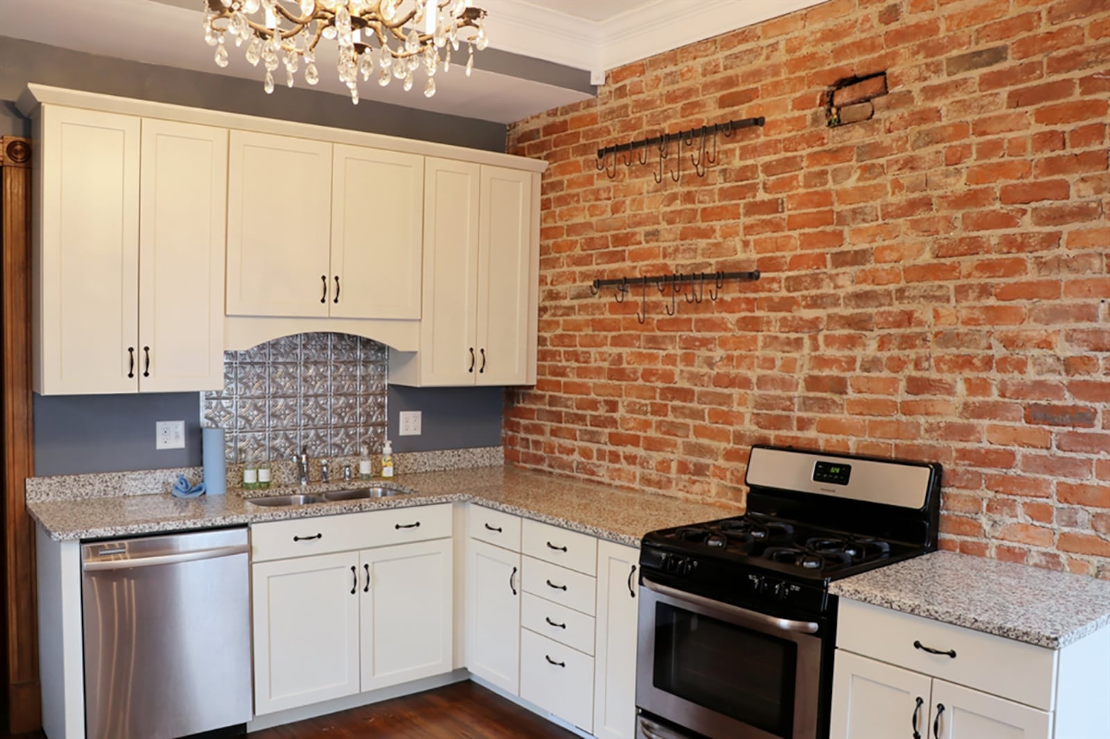 The kitchen has been redesigned to its original floor plan. An exposed brick wall accents the antique white cabinetry and granite countertops. A pantry cabinet surrounds the refrigerator, and stainless-steel appliances include a range and dishwasher. CONTRIBUTED PHOTO BY KATHY TYLER