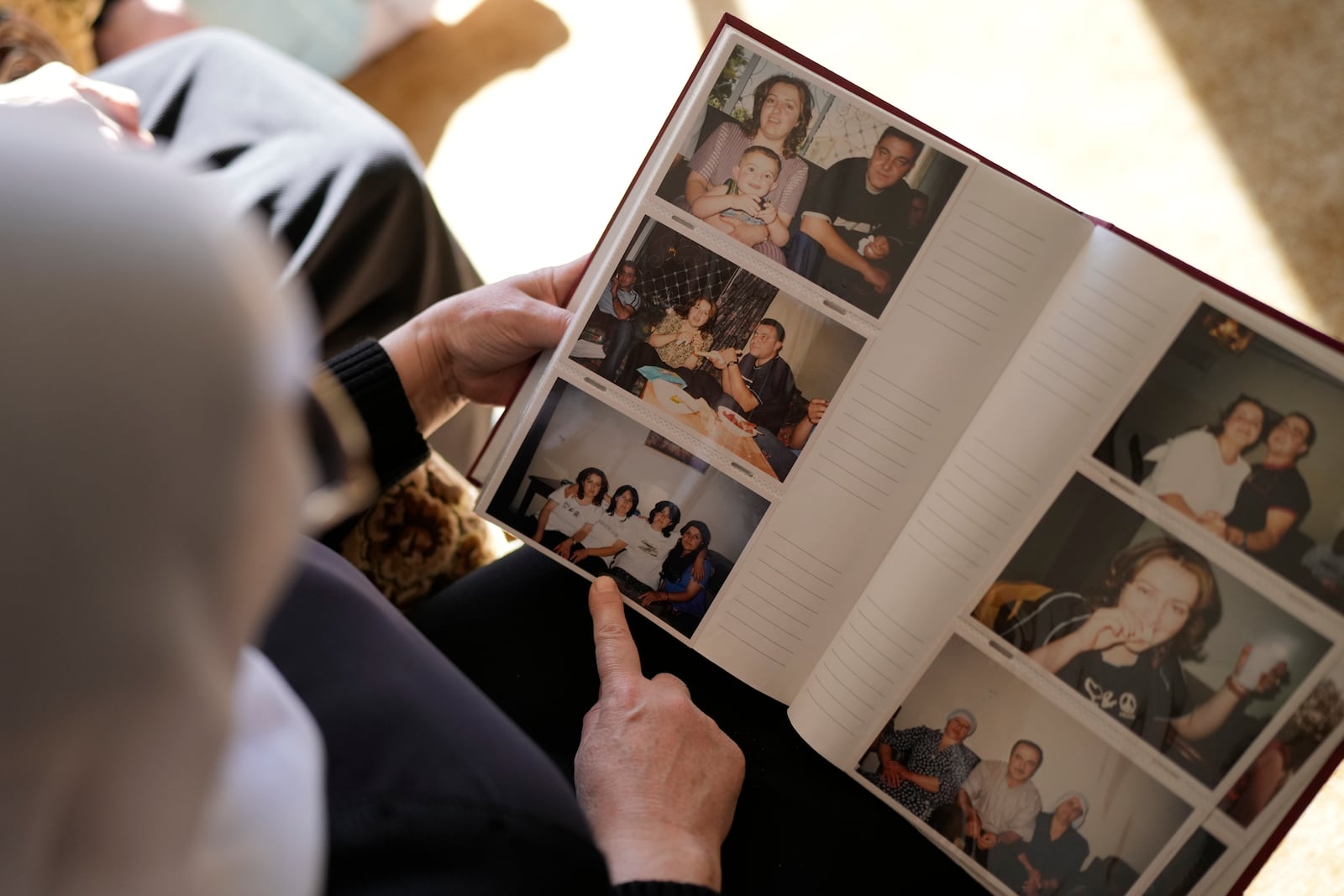 Samar Safadi looks at family photos after speaking by phone with her sister, Sawsan, who lives inside the buffer zone near the "Alpha Line" that separates the Israeli-controlled Golan Heights from Syria, in the town of Majdal Shams, Wednesday, Dec. 18, 2024. (AP Photo/Matias Delacroix)