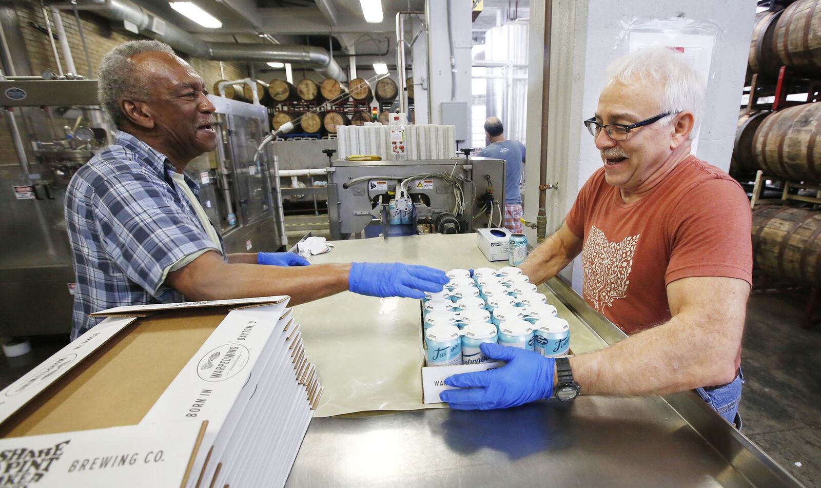 Harold Lovett, left, and packaging manager Kenny Riancho share a laugh as Riancho moves a case of Trotwood Lager at Warped Wing Brewing Company in Dayton. TY GREENLEES / STAFF