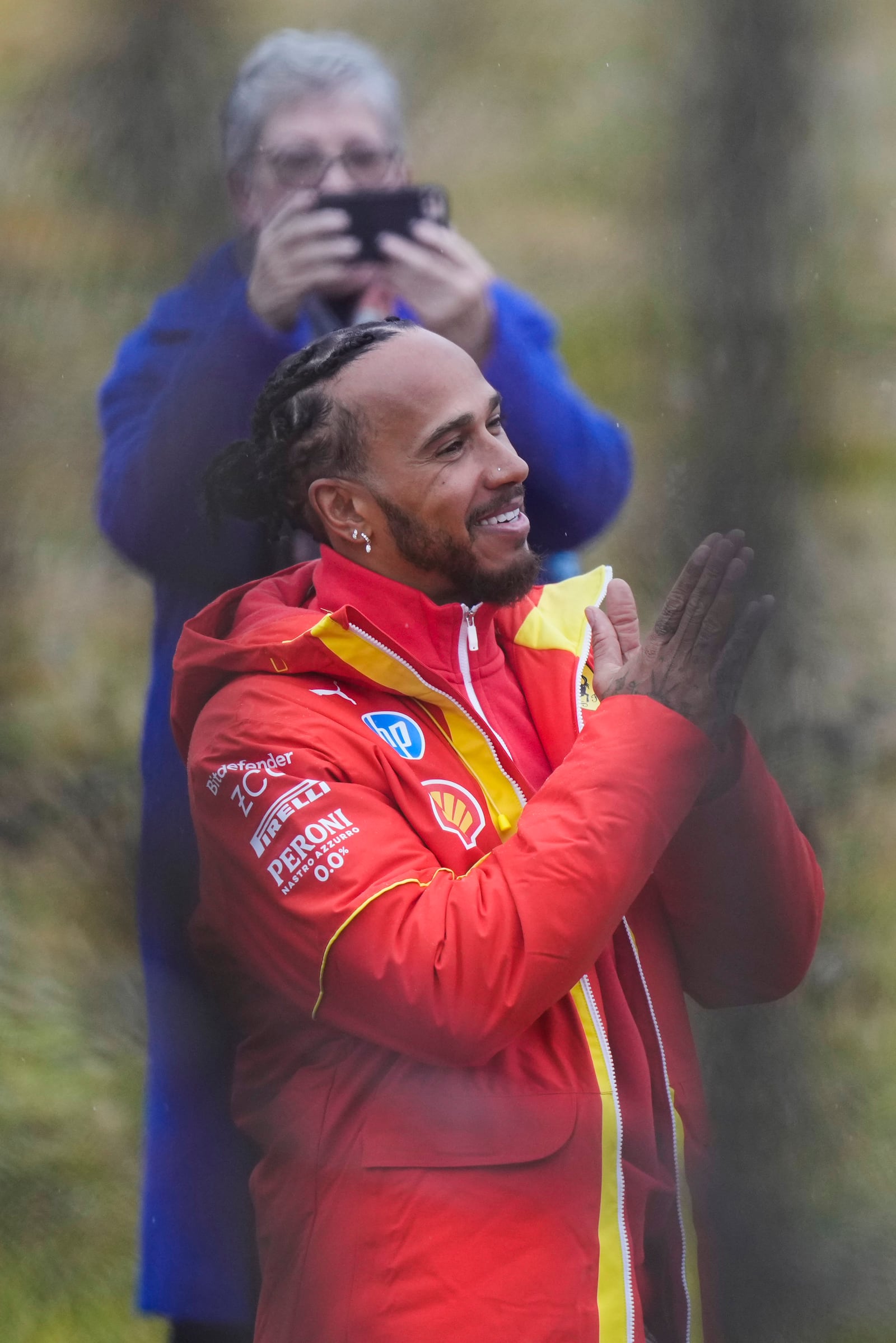 British driver Lewis Hamilton cheers Ferrari fans gathered outside the track, after testing a Ferrari Formula One SF-23, in Fiorano Modenese, Italy, Wednesday, Jan.22, 2025. In background Hamilton's mother Carmen Larbalestier takes pictures with her smartphone. (AP Photo/Luca Bruno)