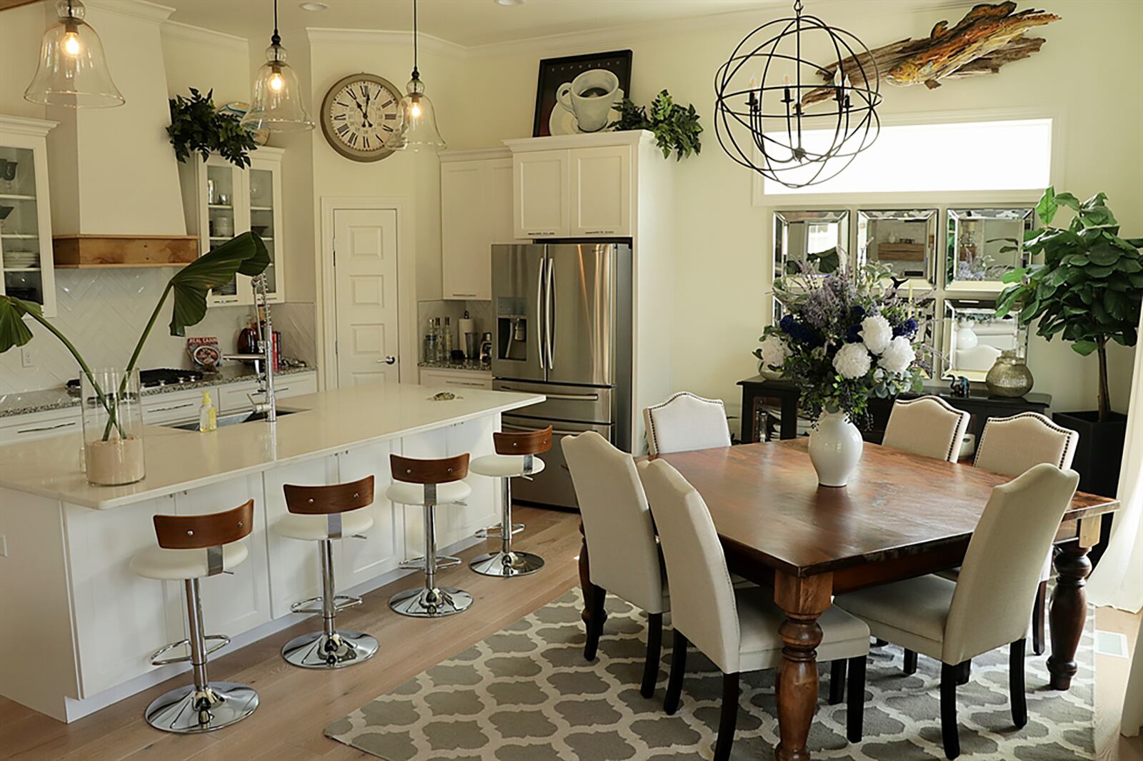 Herringbone-patterned white tile accents the kitchen’s wall space around the hanging glass cabinets and cooking area that has a gas cooktop. There are wall ovens and a stainless-steel refrigerator plus a corner pantry closet. Hanging bell-glass lights hang above the island and a circle wrought-iron chandelier hangs above the dining area. CONTRIBUTED PHOTO BY KATHY TYLER