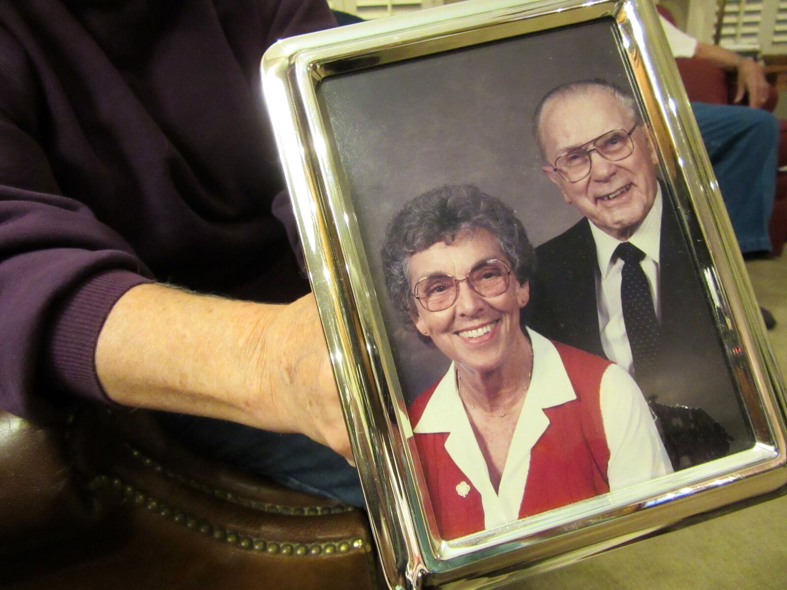 Carolyn Bradfield of Centerville holds a photo of her late parents, Bertha and Charles Murphy. Her mother was victimized by financial scammers when she was 89. LYNN HULSEY / STAFF