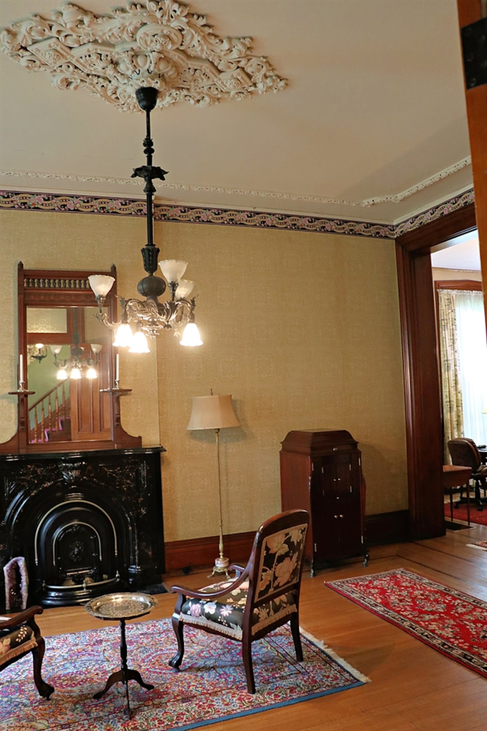 A door opens from the foyer into the parlor. Plaster frieze frames the ceiling plaster medallion; and an iron light fixture has glass tulips.