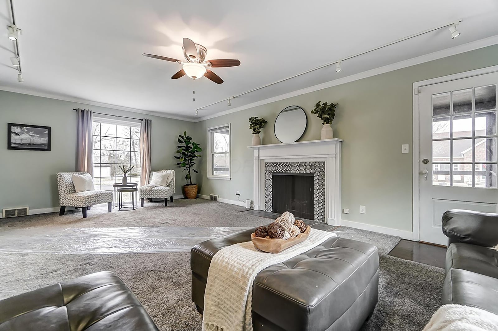 The living room has newer neutral carpeting, a woodburning fireplace, track lighting and a ceiling fan.