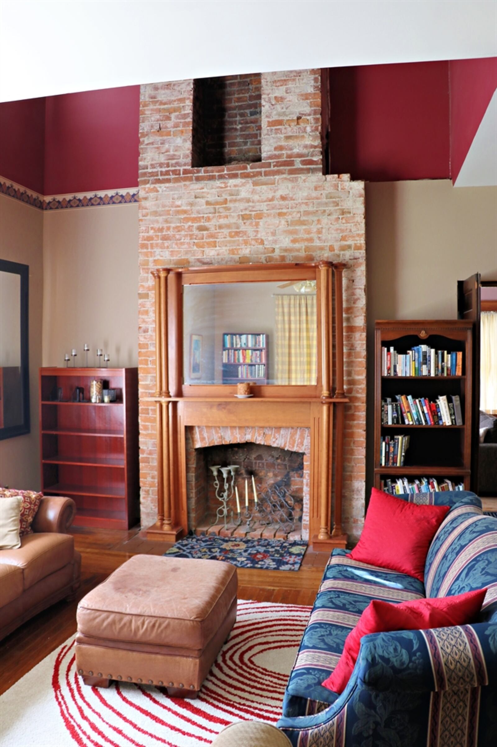 The exposed brick fireplace has a pillar wood mantel and mirror surrounding the fire pit opening, but the brick extends up through a cutout into the second level.