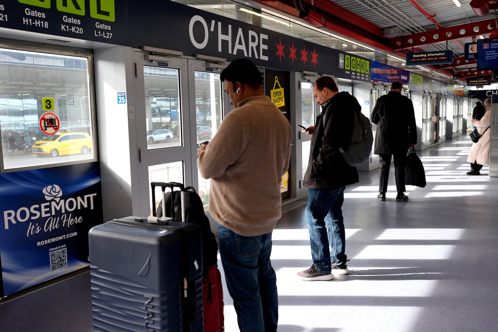 Travelers check their phone as they wait on an airport train to international terminal at O'Hare International Airport in Chicago, Friday, March 21, 2025. (AP Photo/Nam Y. Huh)