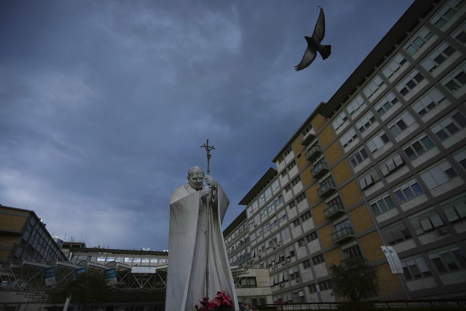 A marble statue of late Pope John Paul II is backdropped by the Agostino Gemelli Polyclinic in Rome, Saturday, Feb. 15, 2025, where Pope Francis was hospitalised Friday after a weeklong bout of bronchitis worsened and is receiving drug therapy for a respiratory tract infection. (AP Photo/Alessandra Tarantino)