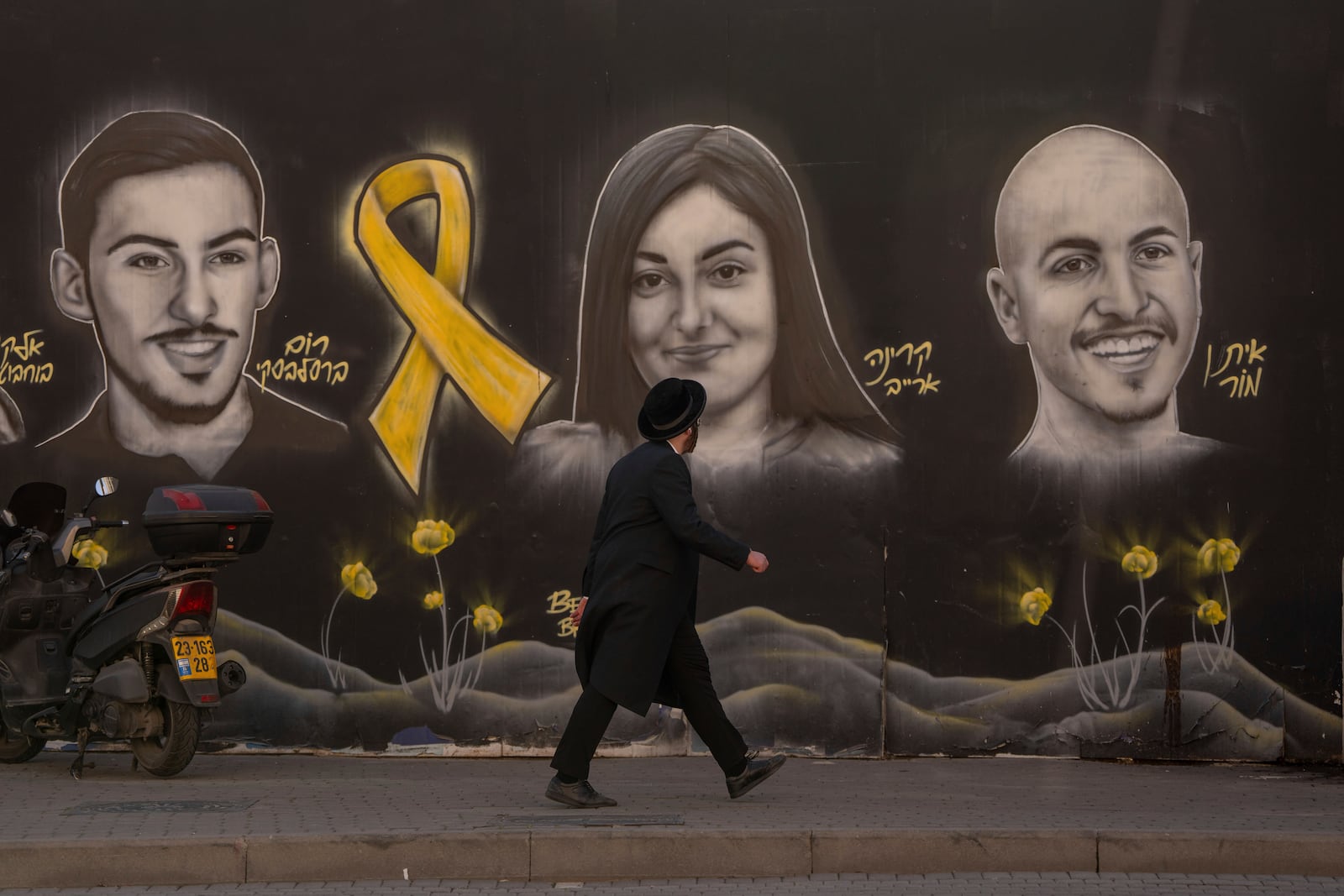 An Ultra-orthodox Jewish man walks past a graffiti that displays portraits of hostages held by Hamas in Gaza, in Jerusalem, on Monday, Jan. 13, 2025. (AP Photo/Ohad Zwigenberg)