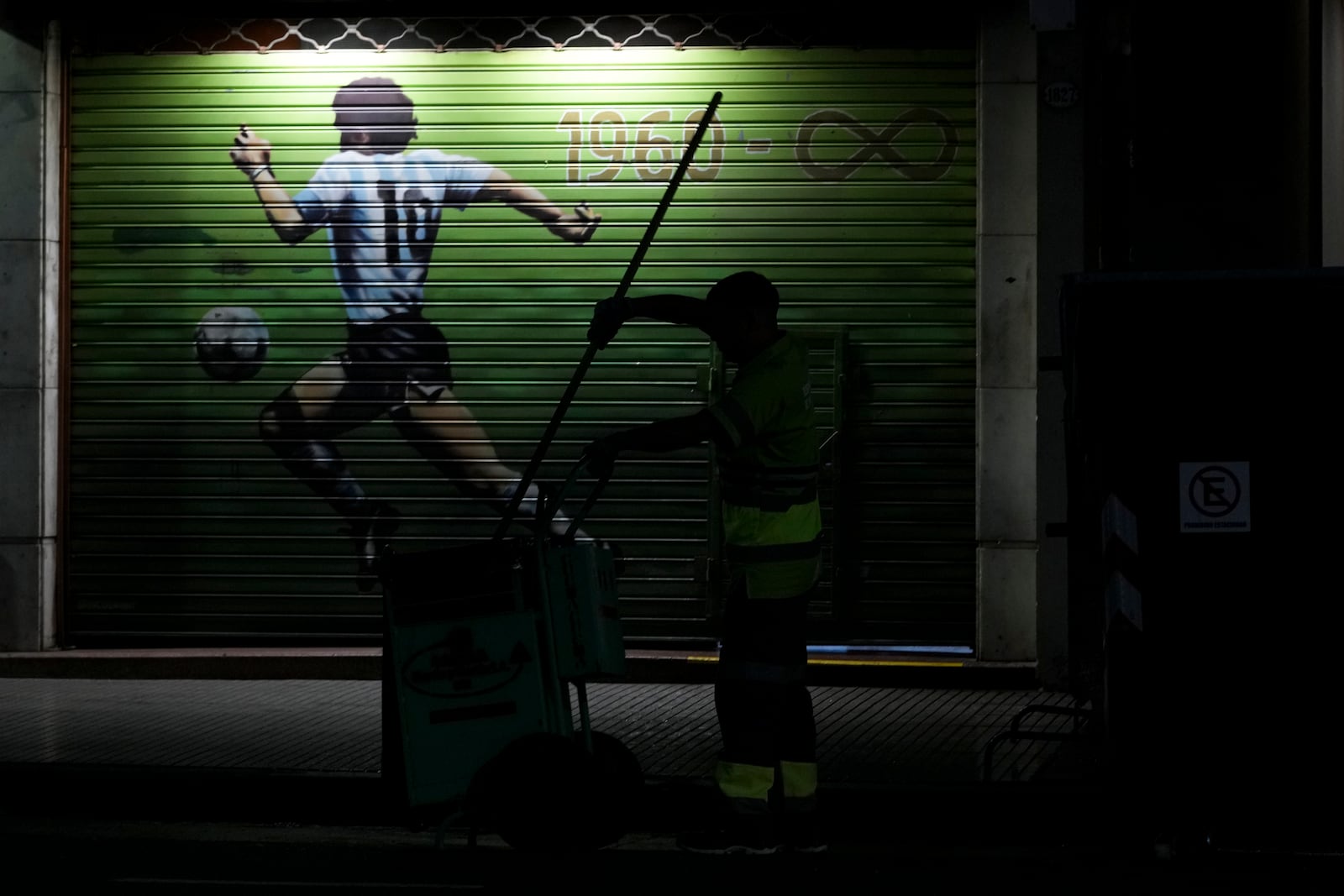 A garbage worker cleans the sidewalk by a mural of late soccer star Diego Maradona in Buenos Aires, Argentina, early Monday, March 10, 2025. (AP Photo/Natacha Pisarenko)