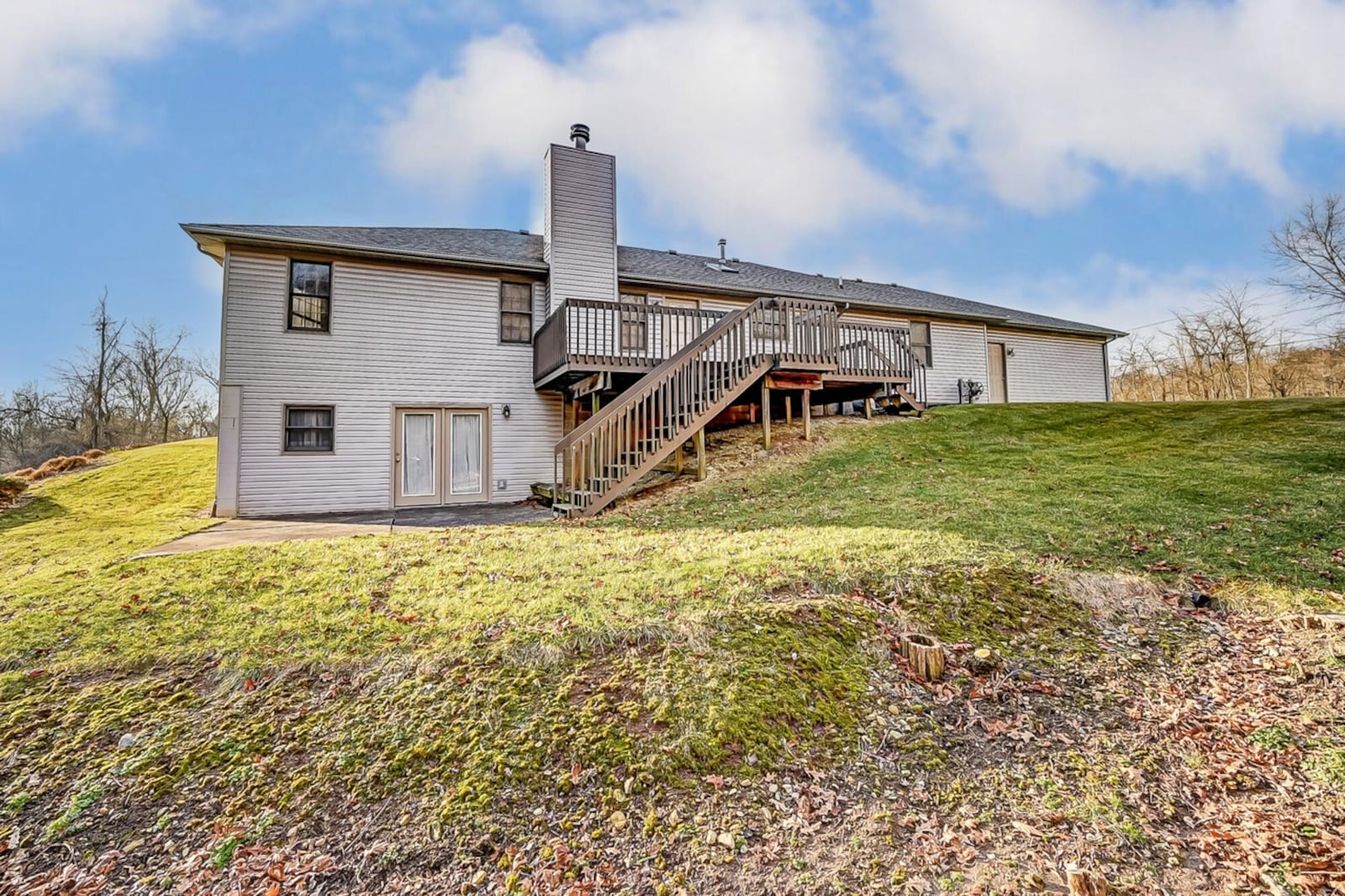 The rear of the home has a wooden deck with railings and steps down to the concrete patio off the walk-out basement