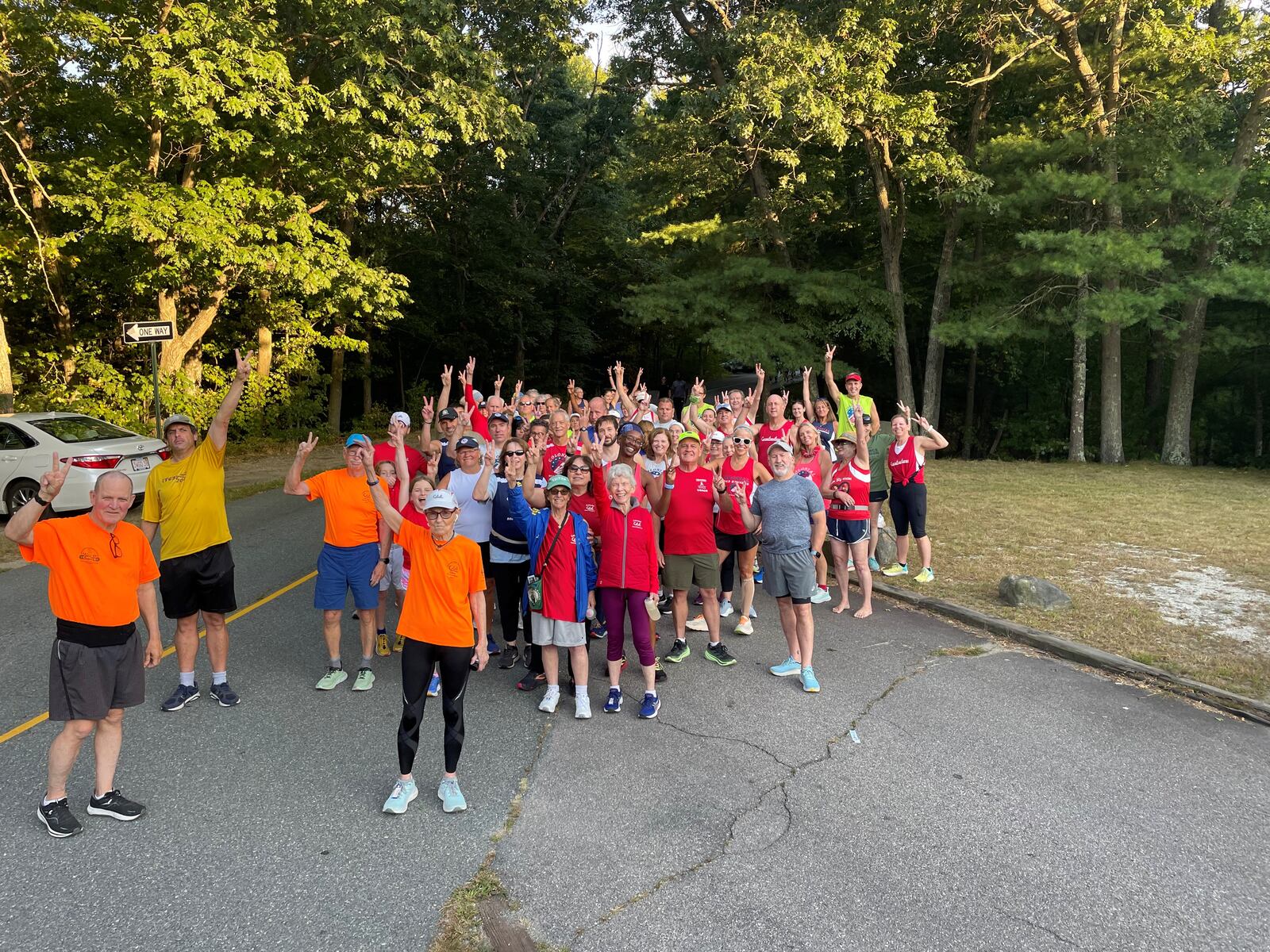 Members of the Colonial Road Runners give one of Mickey Lozan’s traditional peace sign salutes Wednesday evening in Brockton, Massachusetts as they prepare to take part in a Life Celebration Run honoring Lozan, their fellow clubmate, who died suddenly Sept. 1. CONTRIBUTED