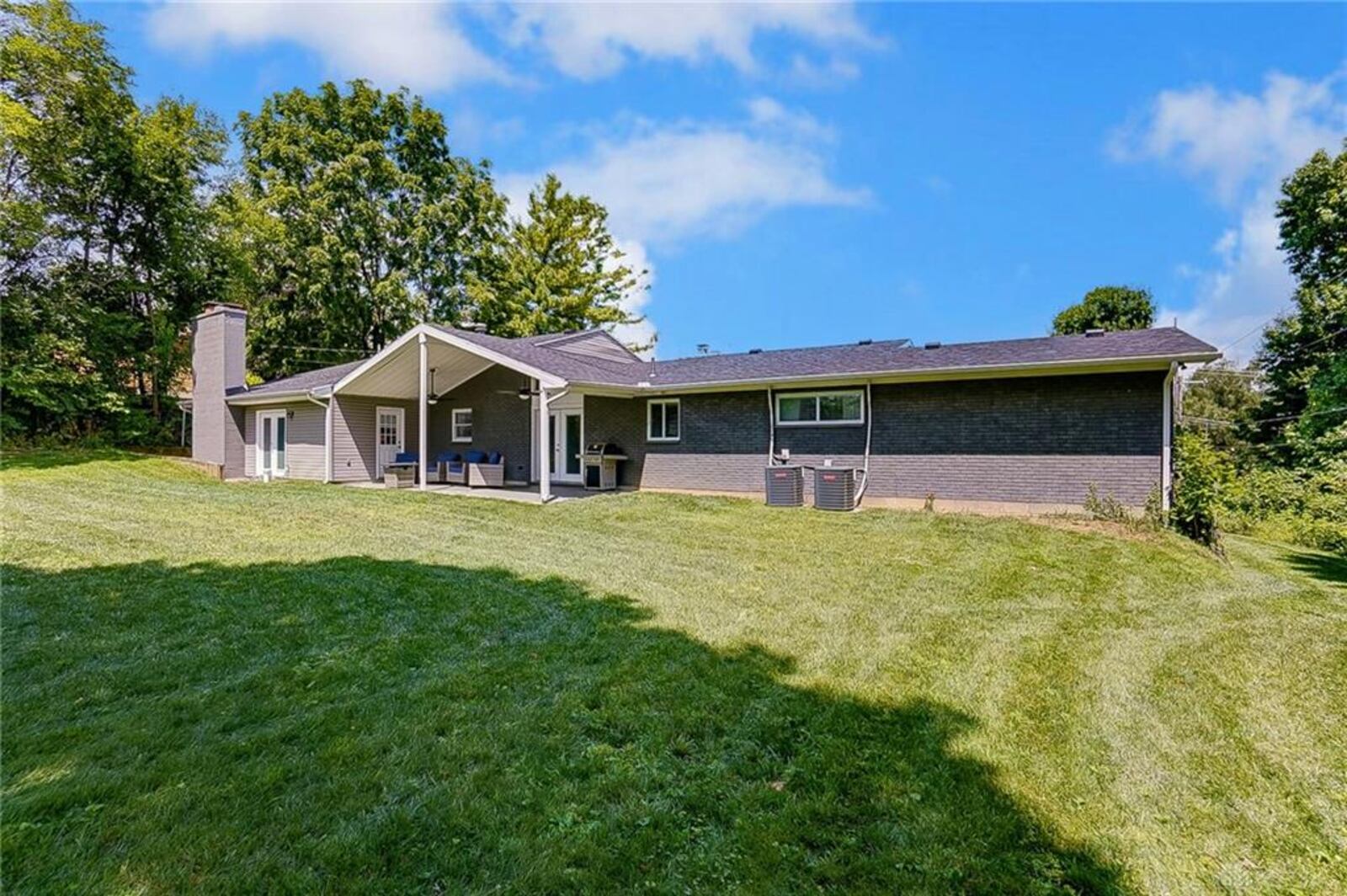 The rear of the home has a family room addition, covered rear concrete porch and tree-lined backyard.