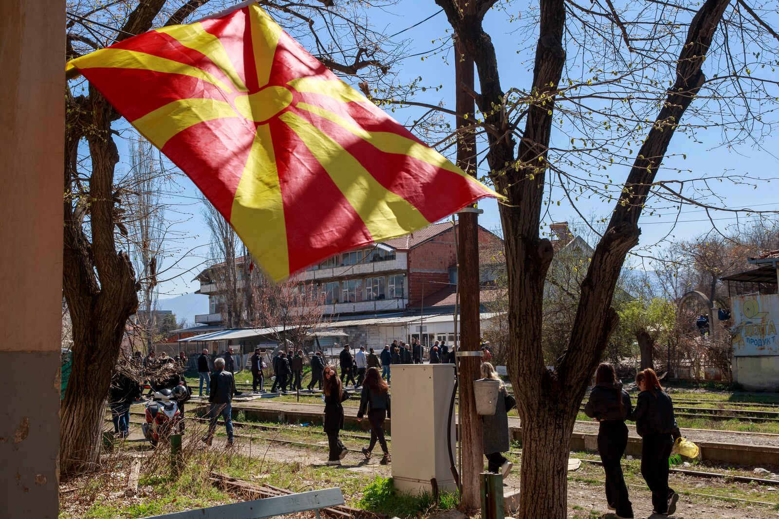 A Macedonian flag is lowered at half mast as people walk along railway tracks, heading for the funeral ceremony of the victims of a massive nightclub fire in the town of Kocani, North Macedonia, Thursday, March 20, 2025. (AP Photo/Visar Kryeziu)