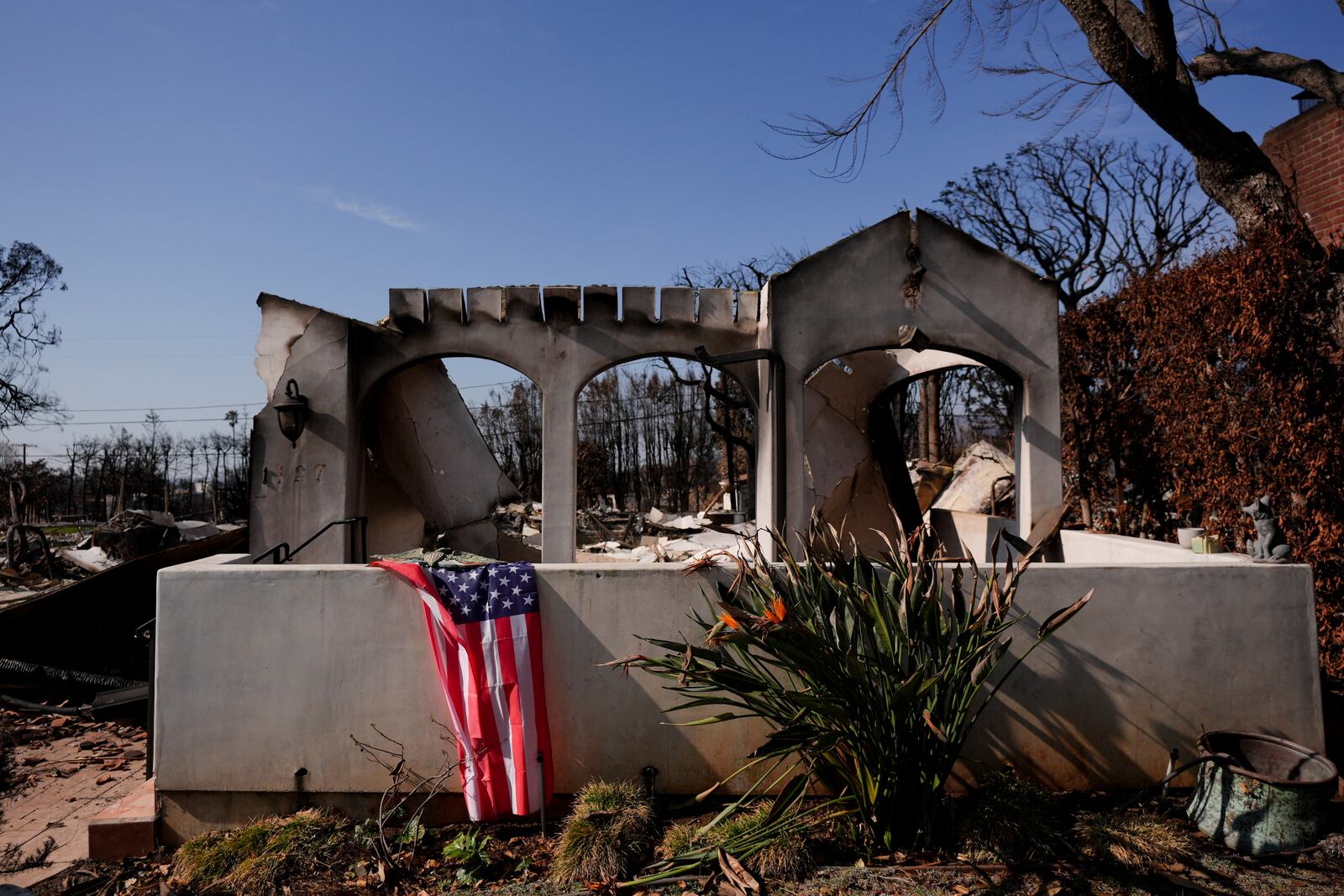 A U.S. flag is draped in front of a fire-ravaged property in the Palisades Fire burn zone in the Pacific Palisades neighborhood of Los Angeles, Tuesday, Jan. 28, 2025. (AP Photo/Jae C. Hong)