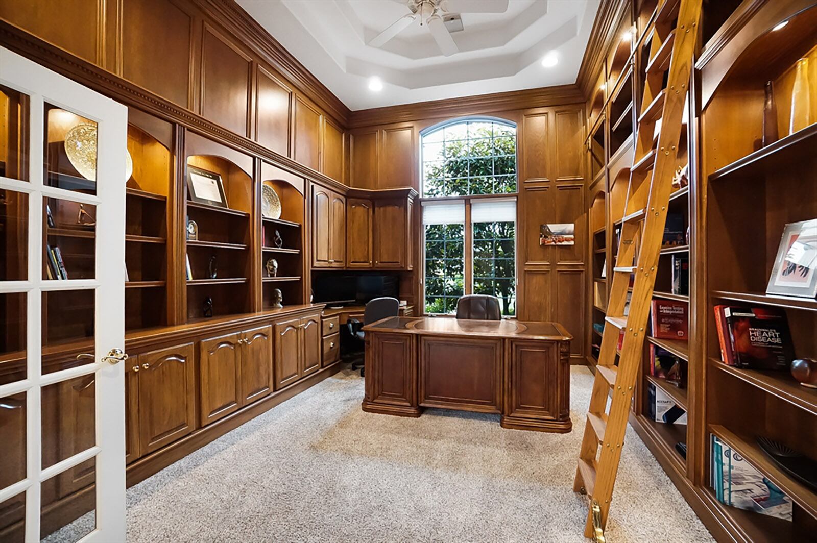 Tucked off the foyer through French doors is the library with rich wood wainscoting, built-in cabinetry, an executive desk, a double tray ceiling and a wall of bookcases with movable library ladder. CONTRIBUTED PHOTO