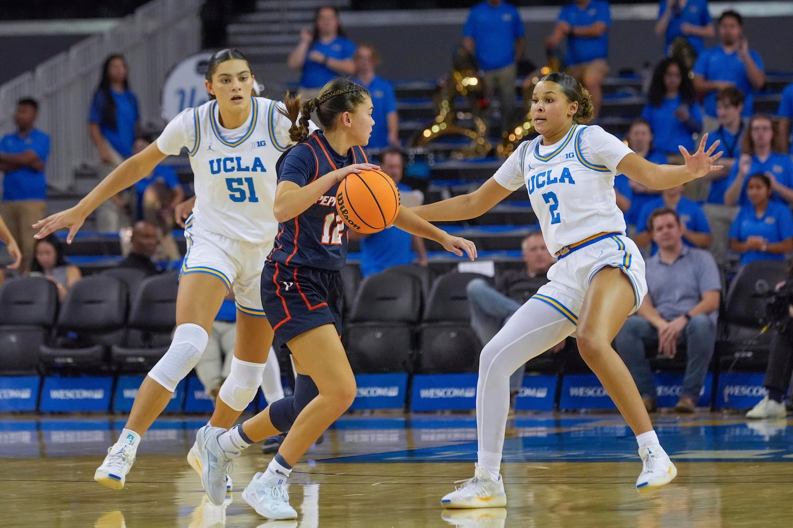 Pepperdine guard Makena Mastora (12) center, attacks against UCLA center Lauren Betts (51) and UCLA guard Avary Cain (2) during a women's NCAA college basketball game, Tuesday, Nov. 12, 2024, in Los Angeles. (AP Photo/Damian Dovarganes)