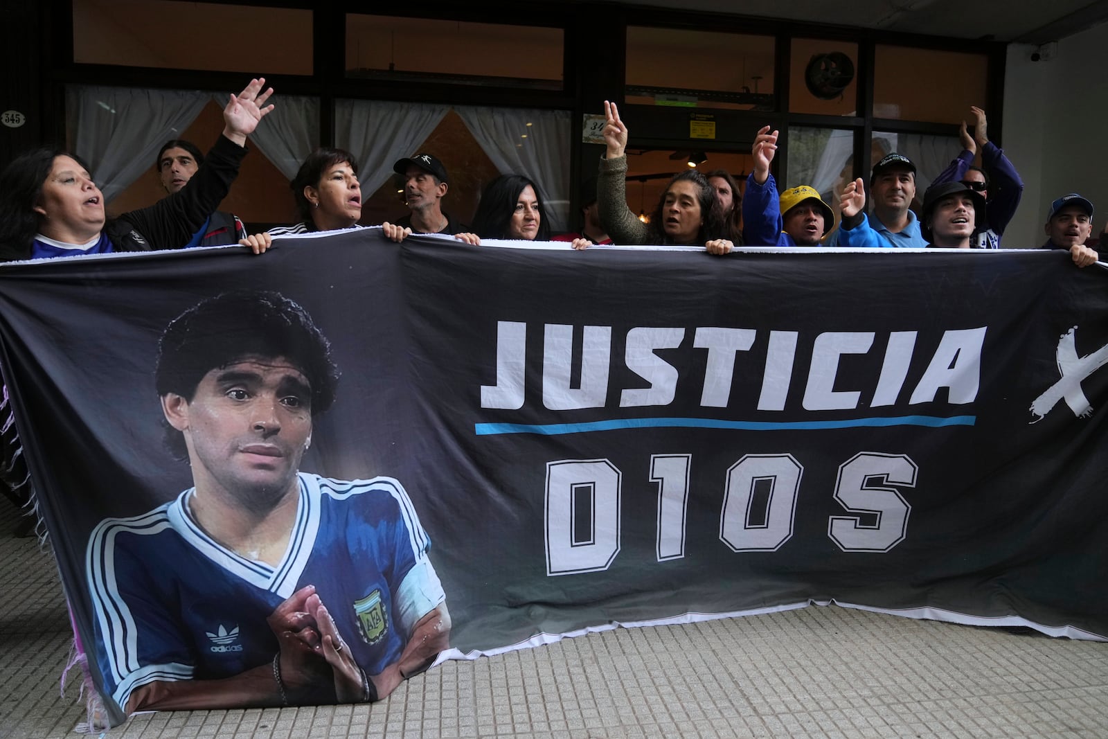 Fans of the late soccer star Diego Maradona hold a banner that reads in Spanish "Justice for God" outside the court where members of the medical team that treated Maradona go on trial for alleged homicide by negligence in San Isidro on the outskirts of Buenos Aires, Argentina, Tuesday, March 11, 2025. (AP Photo/Natacha Pisarenko)