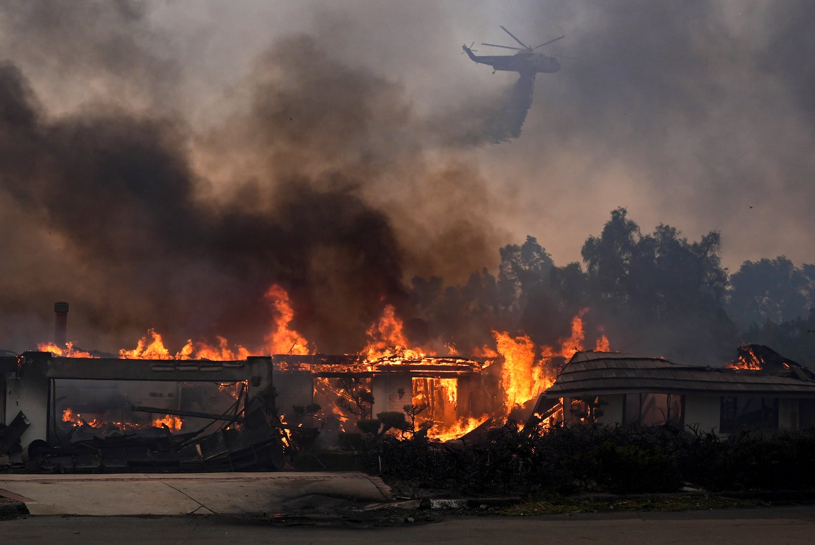 A helicopter drops water over a burning home in the Mountain fire, Wednesday, Nov. 6, 2024, near Camarillo, Calif. (AP Photo/Marcio Jose Sanchez)