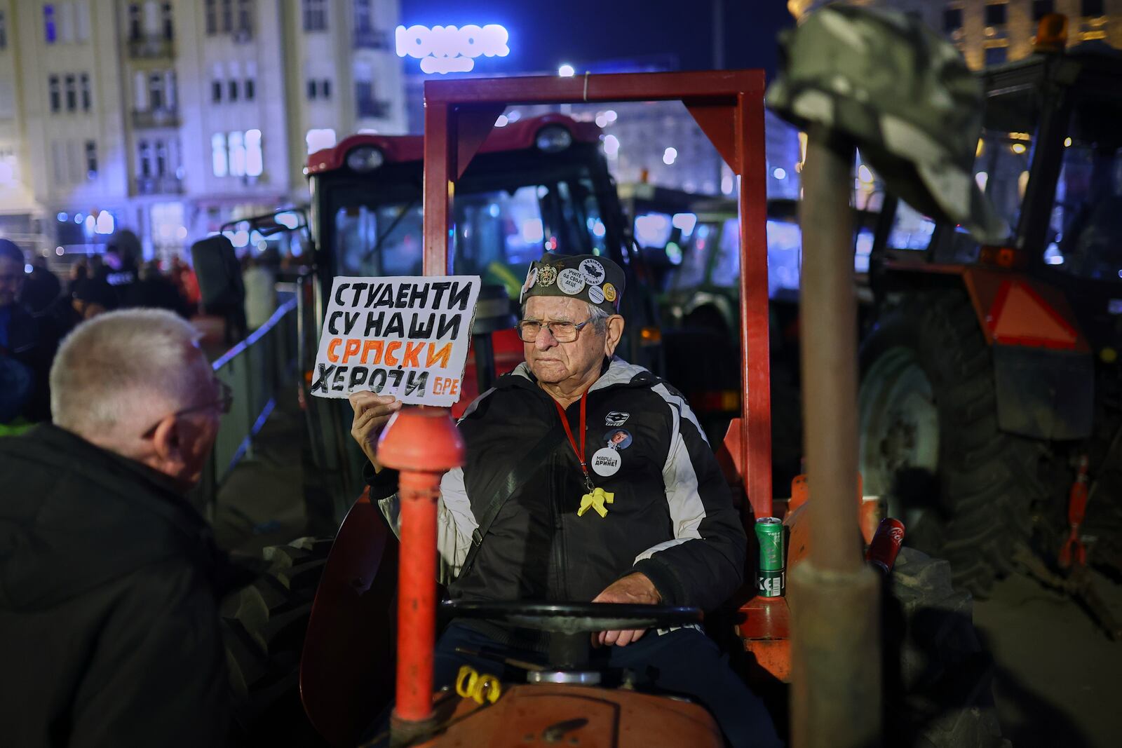 A man holding a placard sits on a tractor as people welcome students who have arrived ahead of a major rally this weekend in downtown Belgrade, Serbia, Friday, March 14, 2025. The placard reads 'Students are our Serbian heroes'. (AP Photo/Armin Durgut)