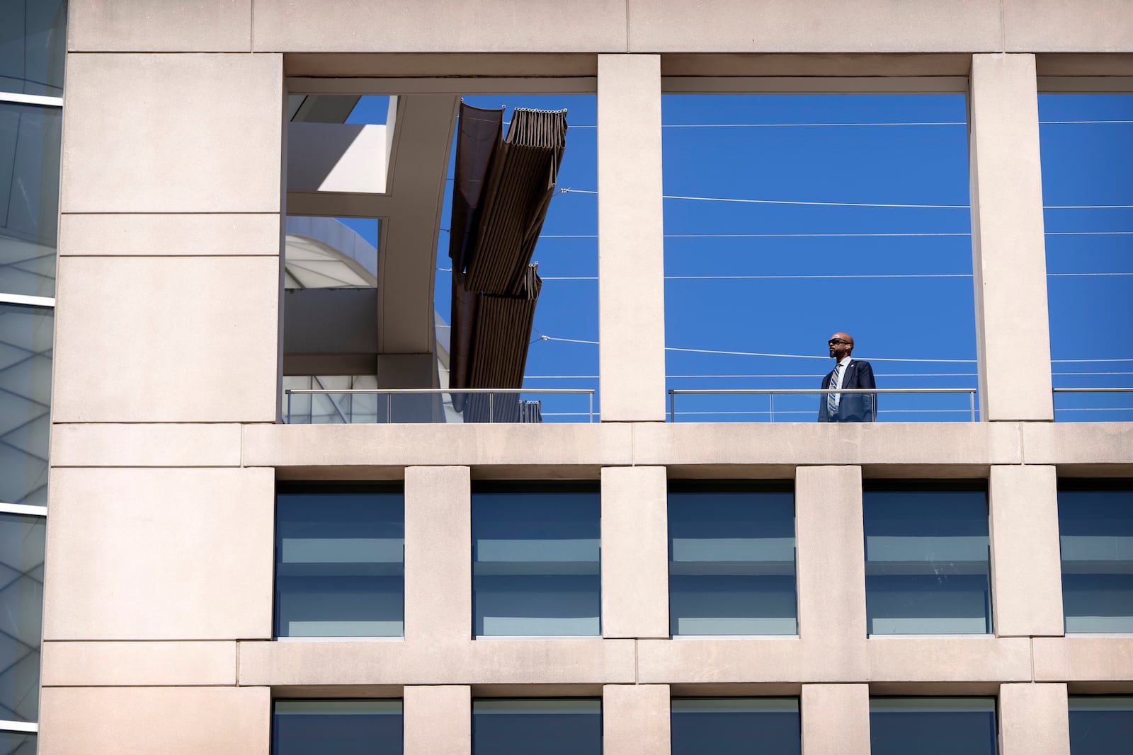 A man wearing an earpiece stands on a balcony at the headquarters of the United States Institute of Peace, Tuesday, March 18, 2025, in Washington. (AP Photo/Mark Schiefelbein).